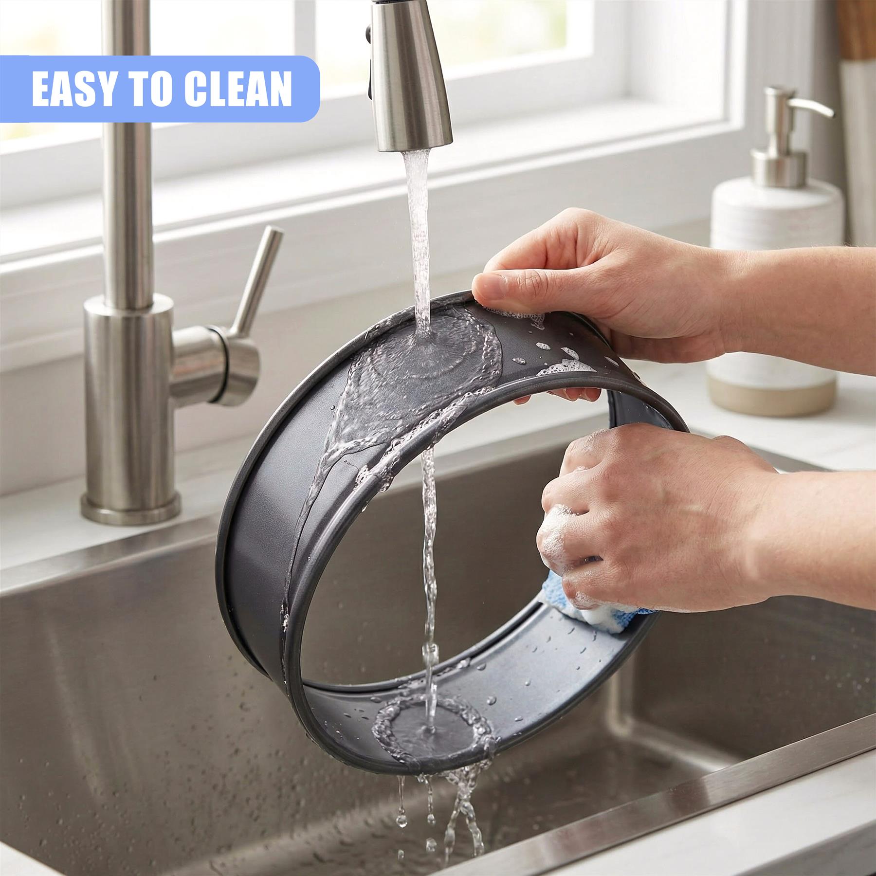 A person washes a metal springform pan in a kitchen sink under running water from a faucet.