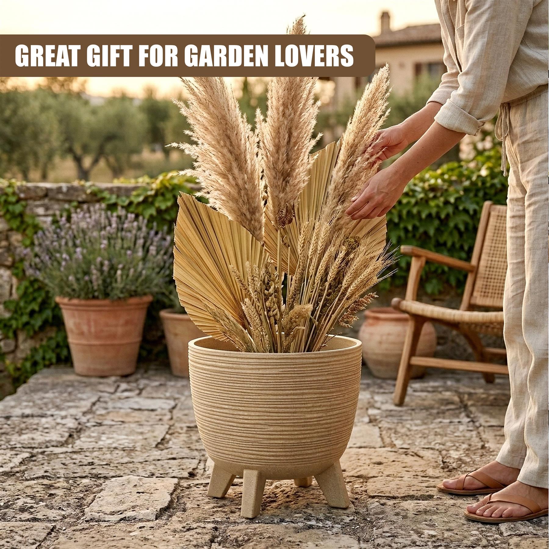 Natural colored pot with legs holds bundled dried reeds and grasses on a stone patio.