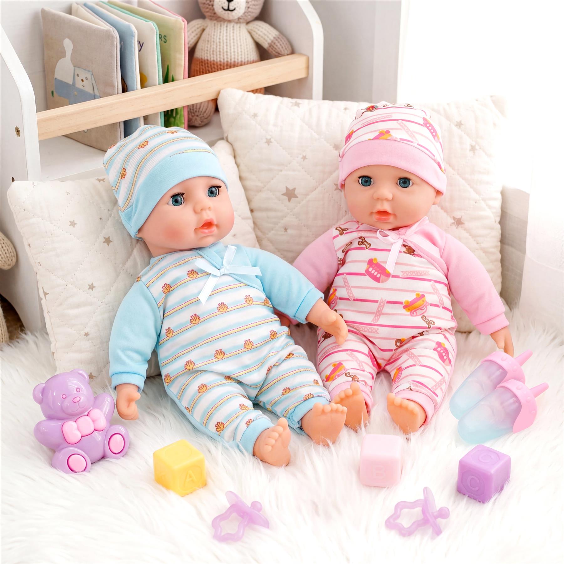 Two dolls in blue and pink clothes are displayed with accessories, toys, and a stuffed bear.