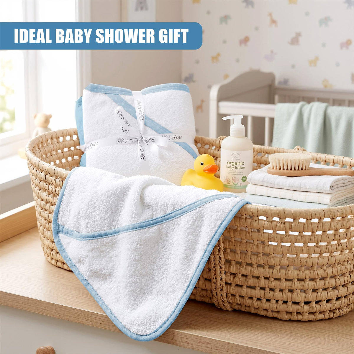 A woven basket contains two hooded GEEZY baby bath towels, a yellow duck and baby lotion