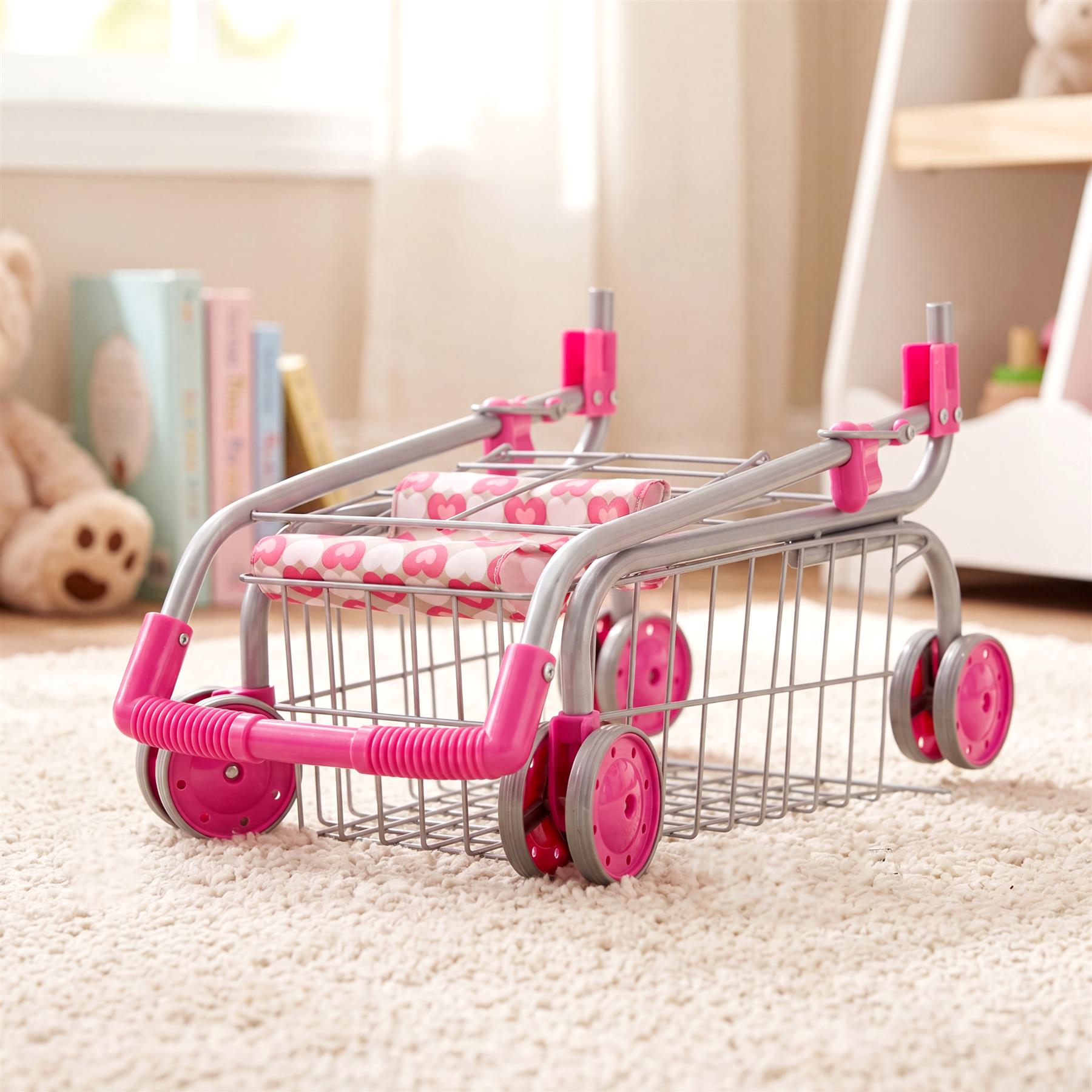 A pink and silver metal kids' shopping trolley featuring a doll seat and four wheels.