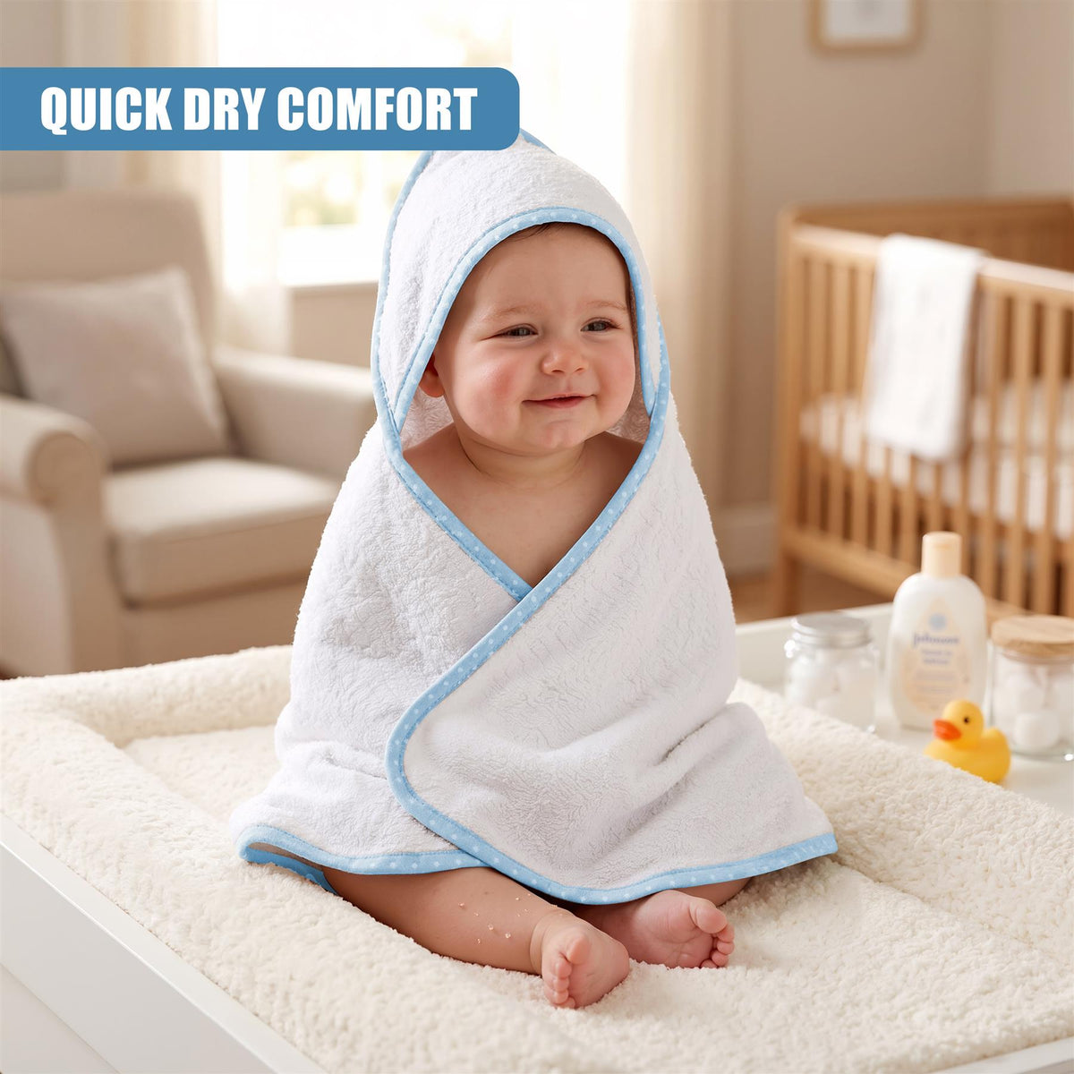 A baby in a blue hooded towel smiles while sitting on a fluffy white towel, part of a set of two GEEZY bath towels