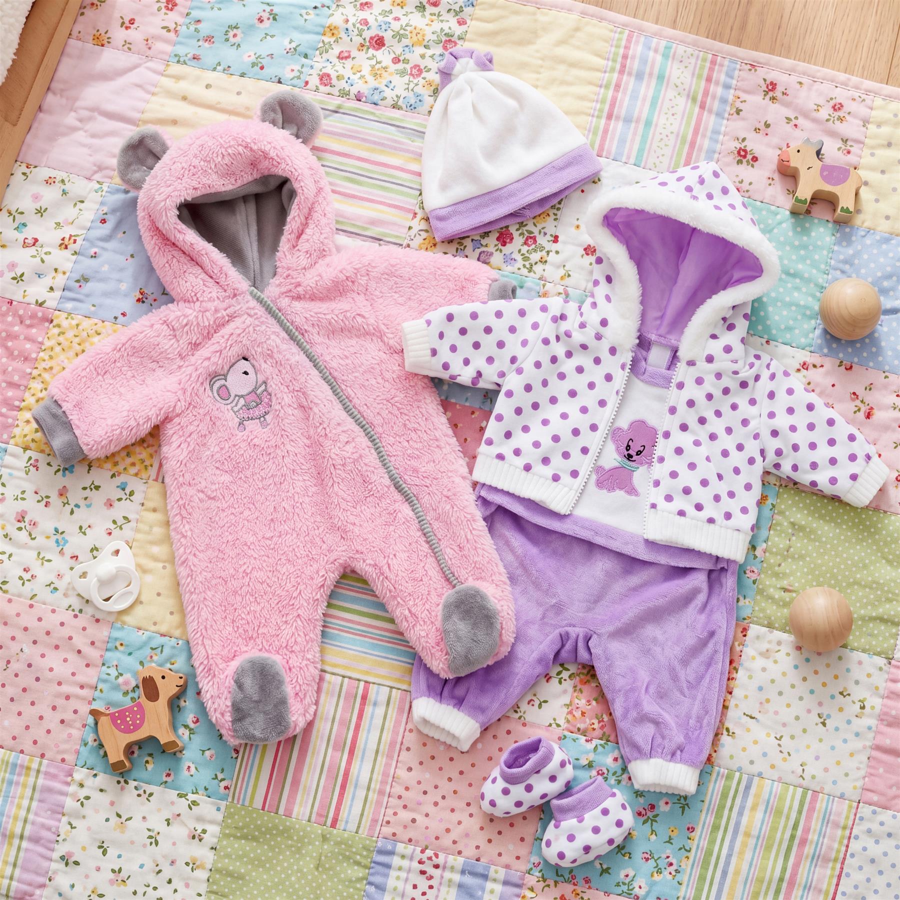 Pink plush bear hooded romper and patterned purple outfit set displayed on a colorful quilt.