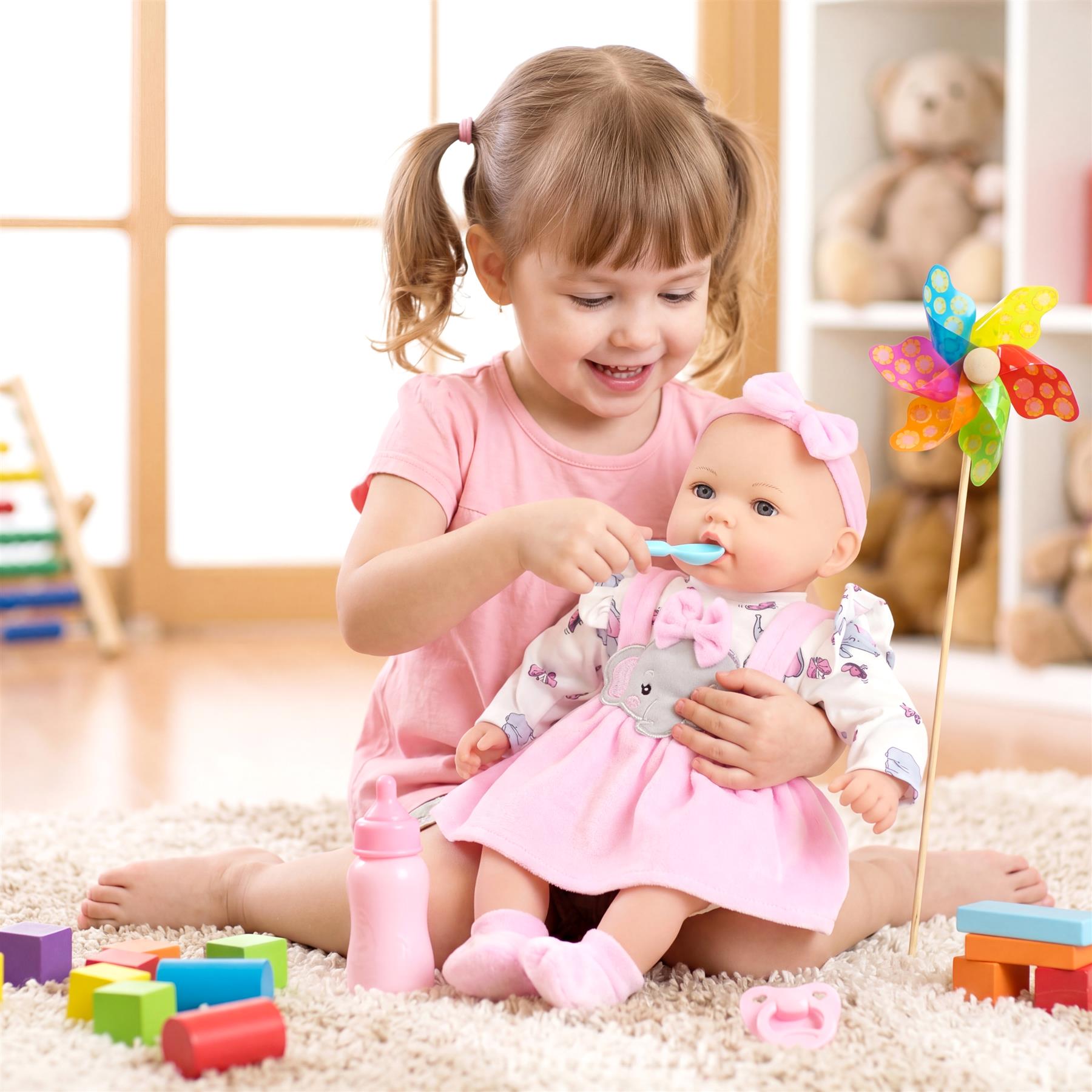 Girl feeds the doll with a spoon while surrounded by building blocks and colorful toys.