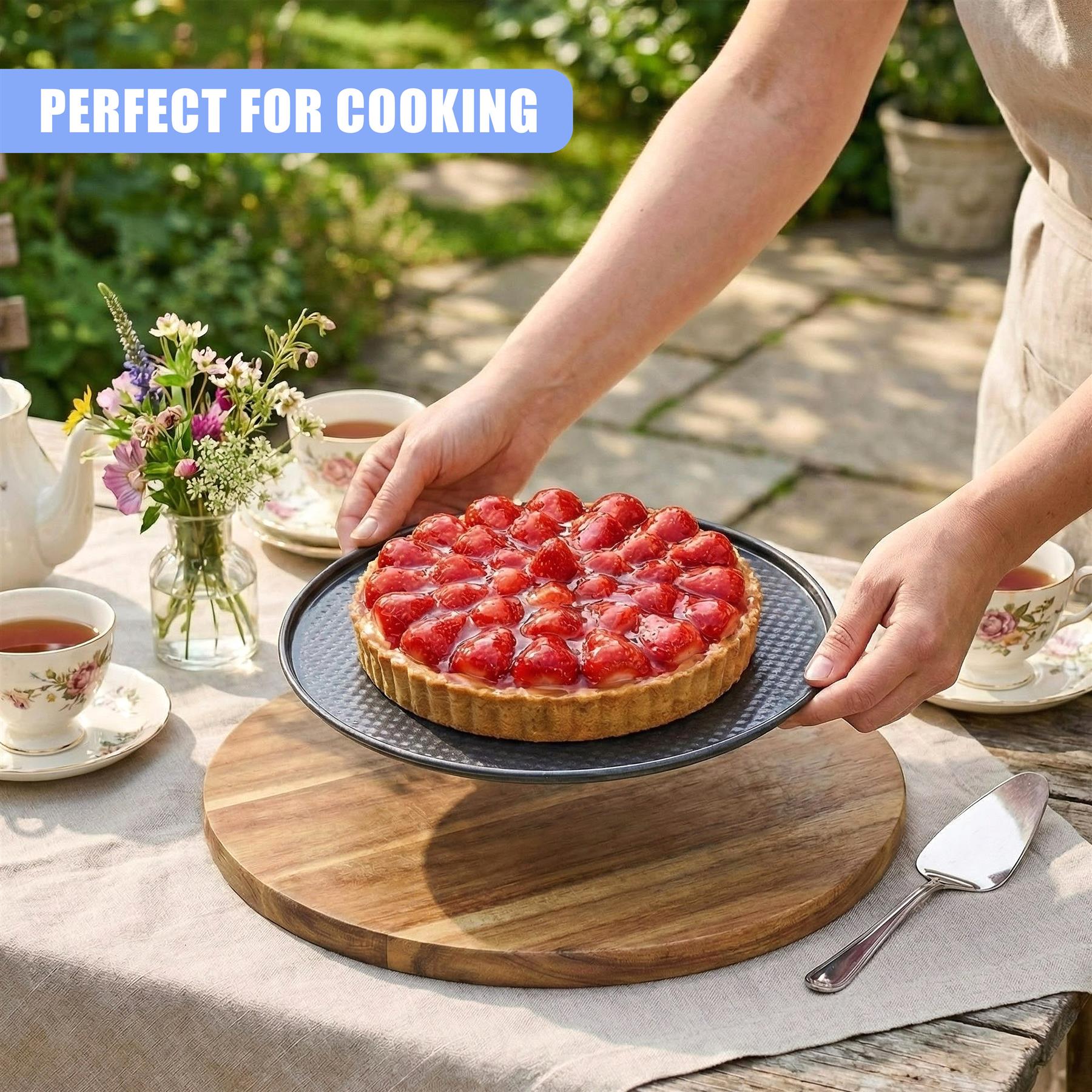 Hands display a finished strawberry cake on a round wooden serving board with baking tools.