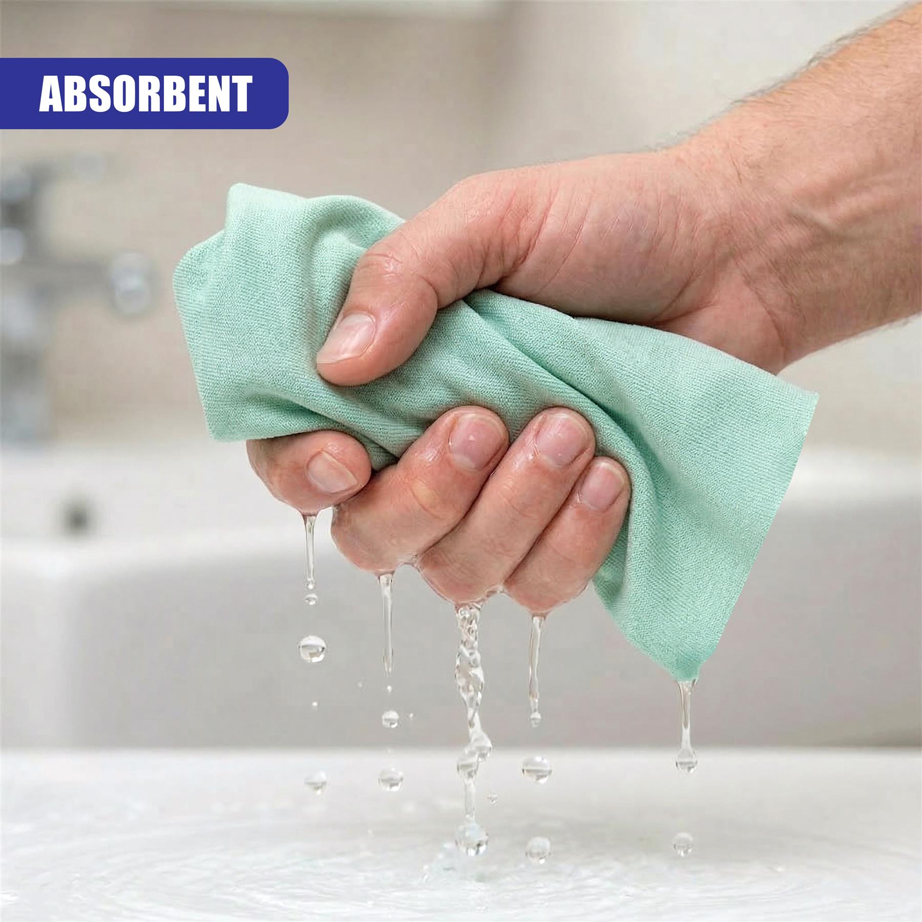 A hand holds a damp, light green cloth dripping water onto a white counter surface.