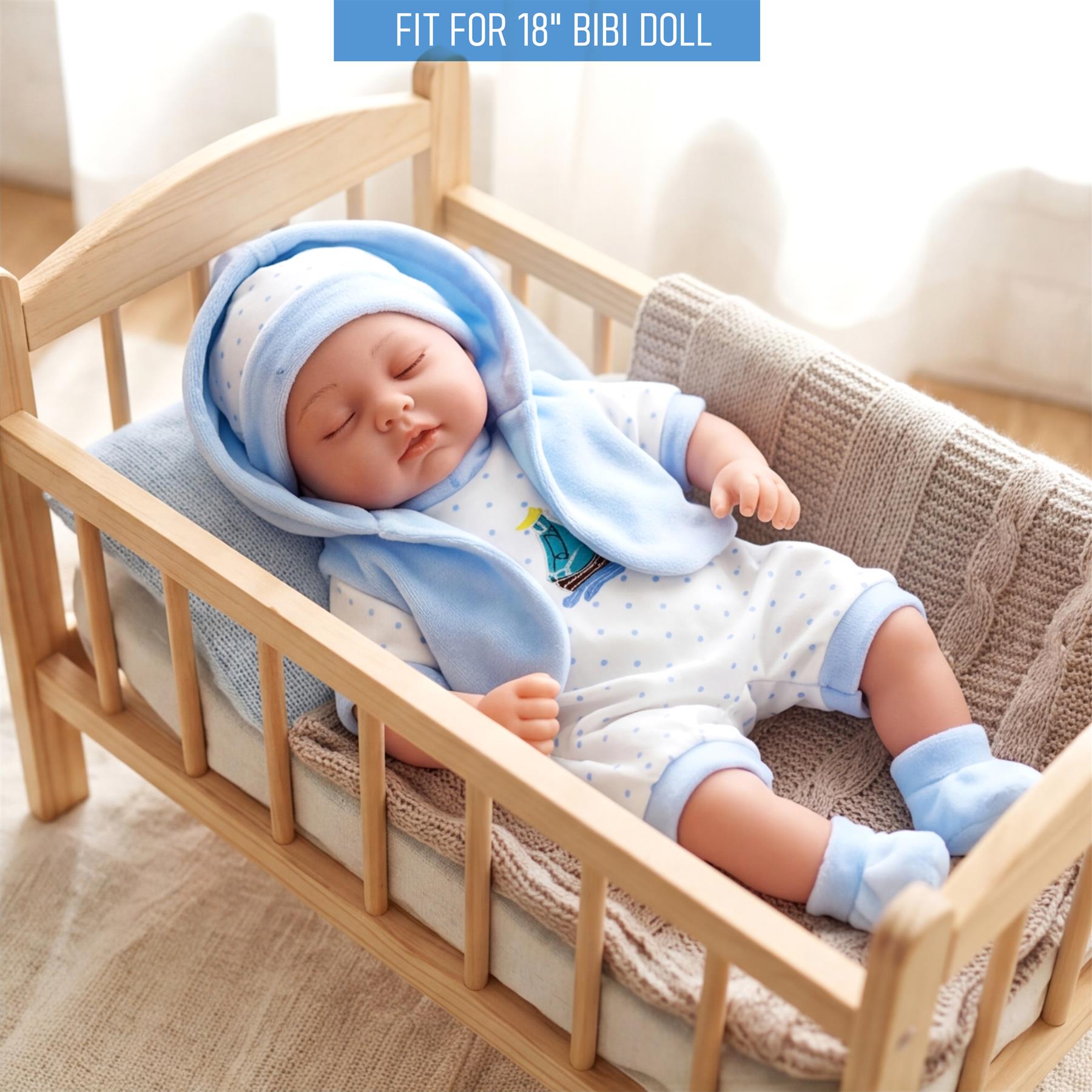 Doll dressed in light blue pajamas and a matching hooded blanket rests in a wooden crib.