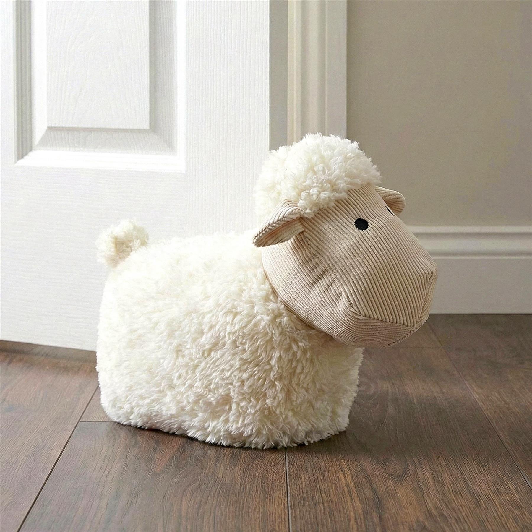 A soft, white, fluffy sheep-shaped doorstop sits on a dark wood floor, with its body resting against a white door. The doorstop's face is made of corduroy, with a black eye and a soft, fluffy, white, curly, and tufted head. The doorstop has a round, fluffy, white tail. The background features a white door and a dark wood floor. - The Magic Toy Shop