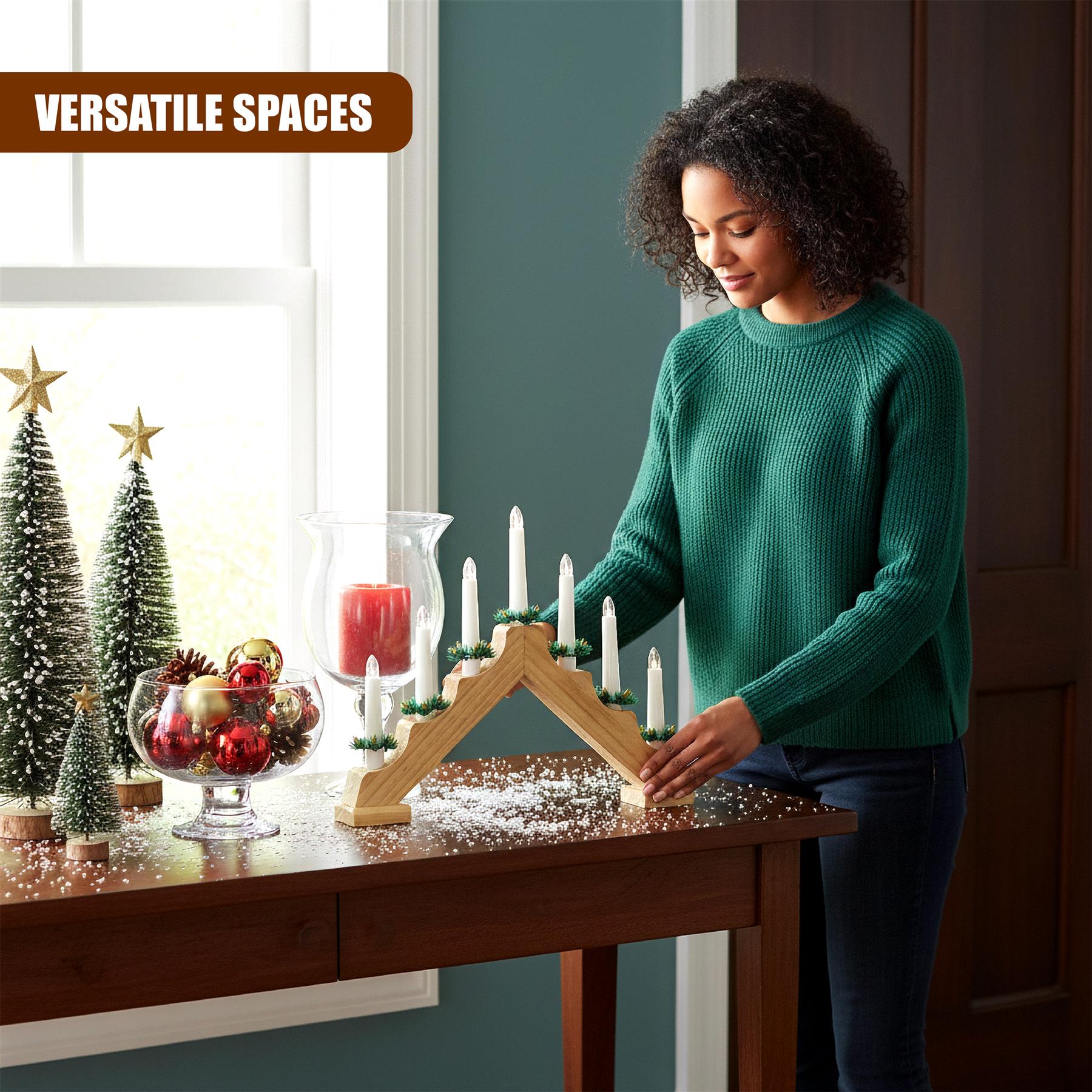 A woman stands beside a wooden, multi-tiered candle holder with white candles and a red candle in the center. The holder is surrounded by Christmas decorations, including small trees, a snow-covered glass bowl with ornaments, and a few pinecones. - The Magic Toy Shop
