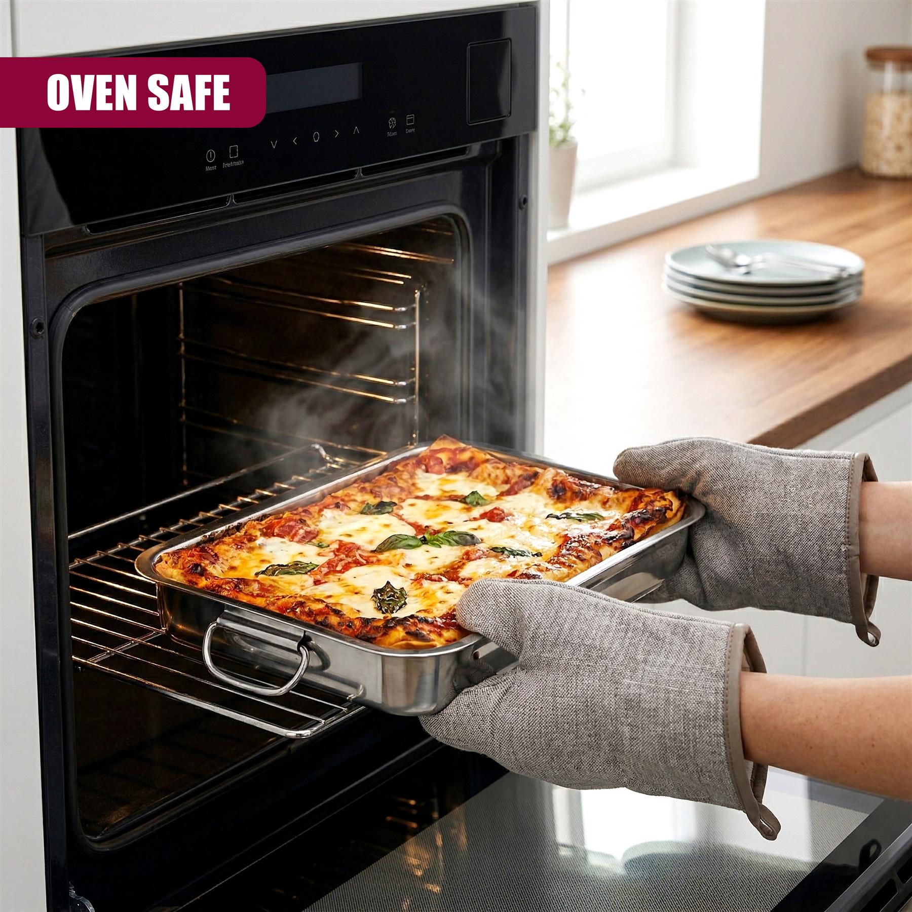 A person removes a cheesy, baked meal from a hot, stainless steel oven tray.