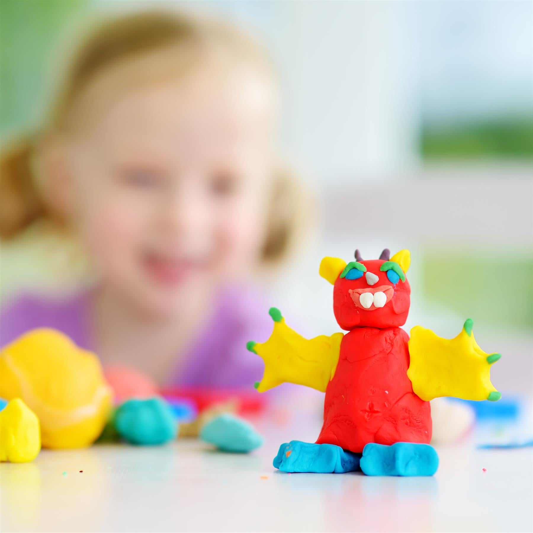 A giant play dough set with a red dinosaur toy sitting on the table.