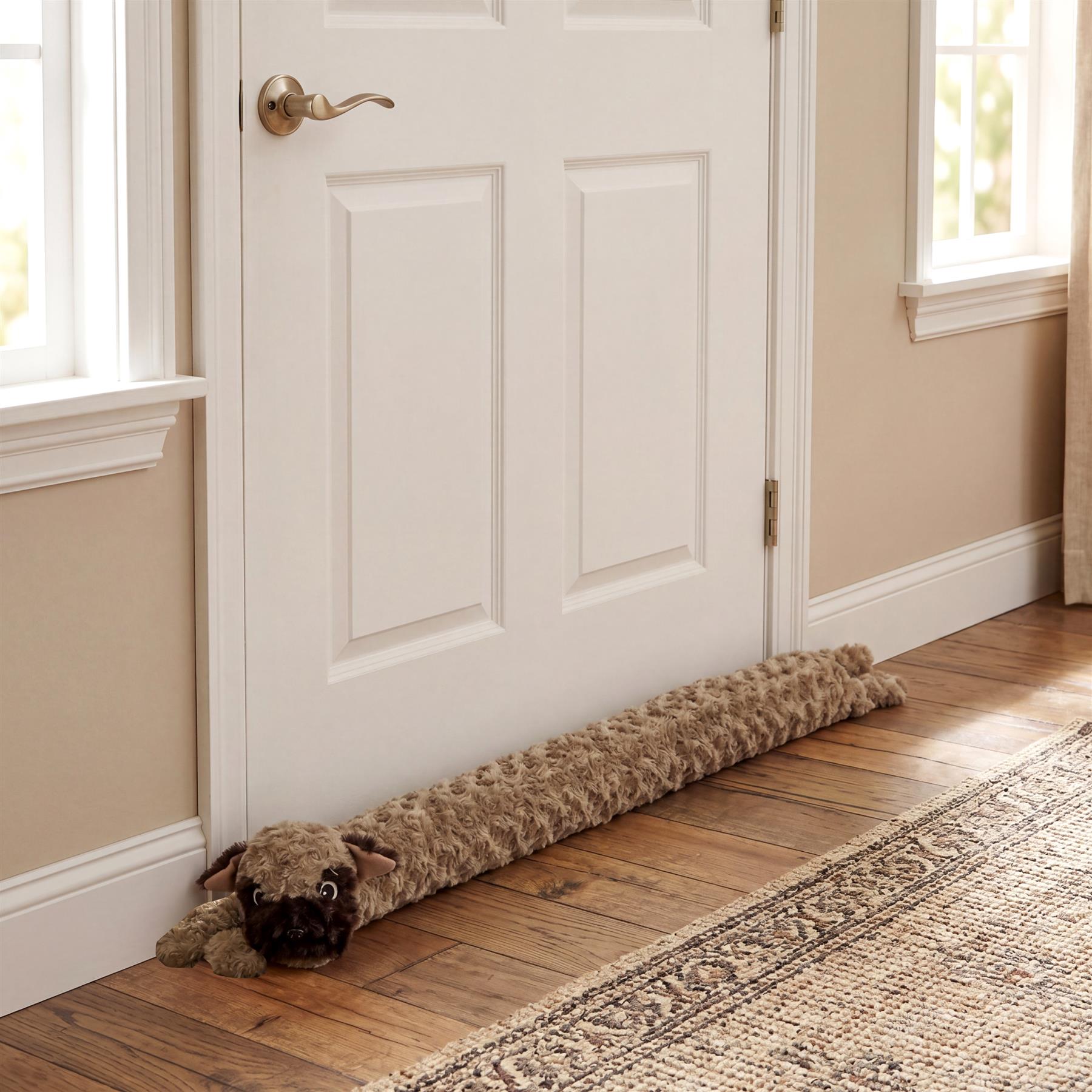 A brown stuffed dog draught excluder rests on a wooden floor on the inner side of a white door.