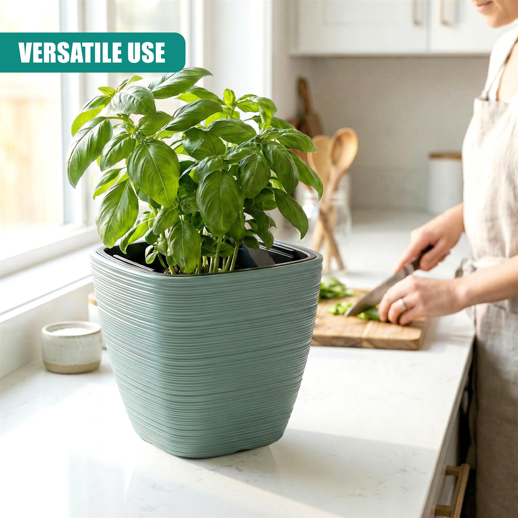 A square, light sage green planter holds a lush plant filled with vibrant green leaves.