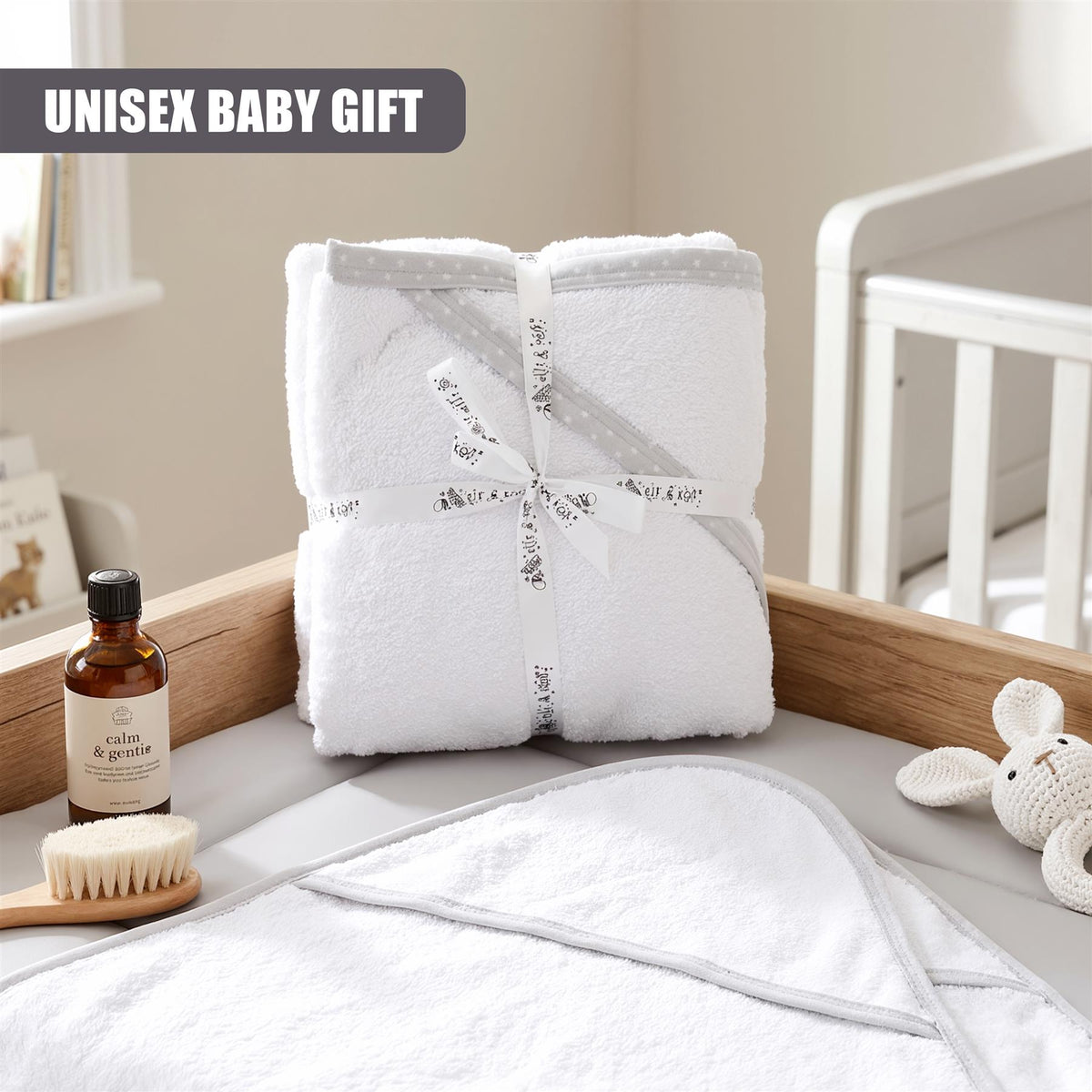 White hooded baby bath towels, part of a two-pack, are presented in a nursery setting with a wooden shelf and a grey doll