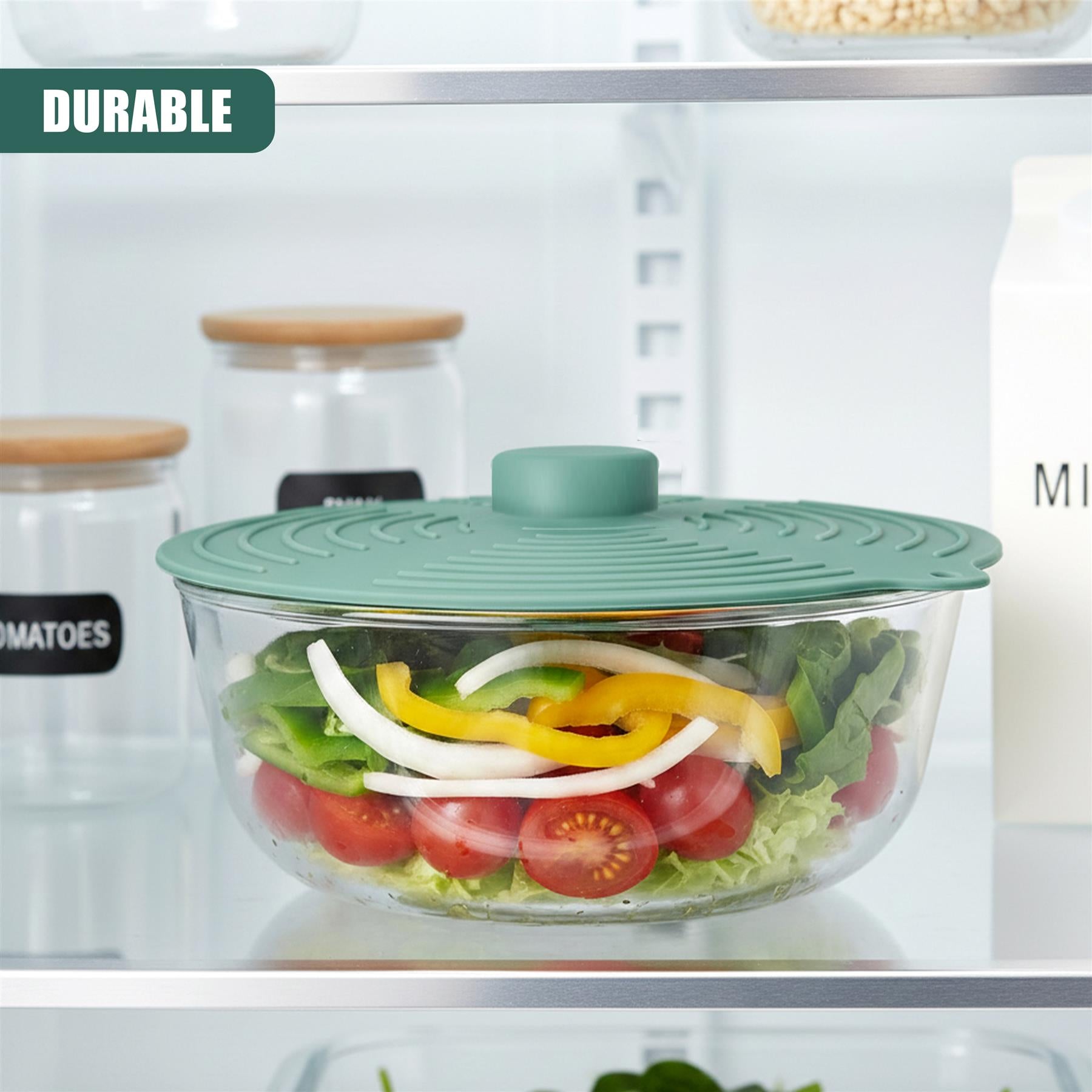 Glass container holding fresh vegetable salad under a teal, silicone, airtight food cover.