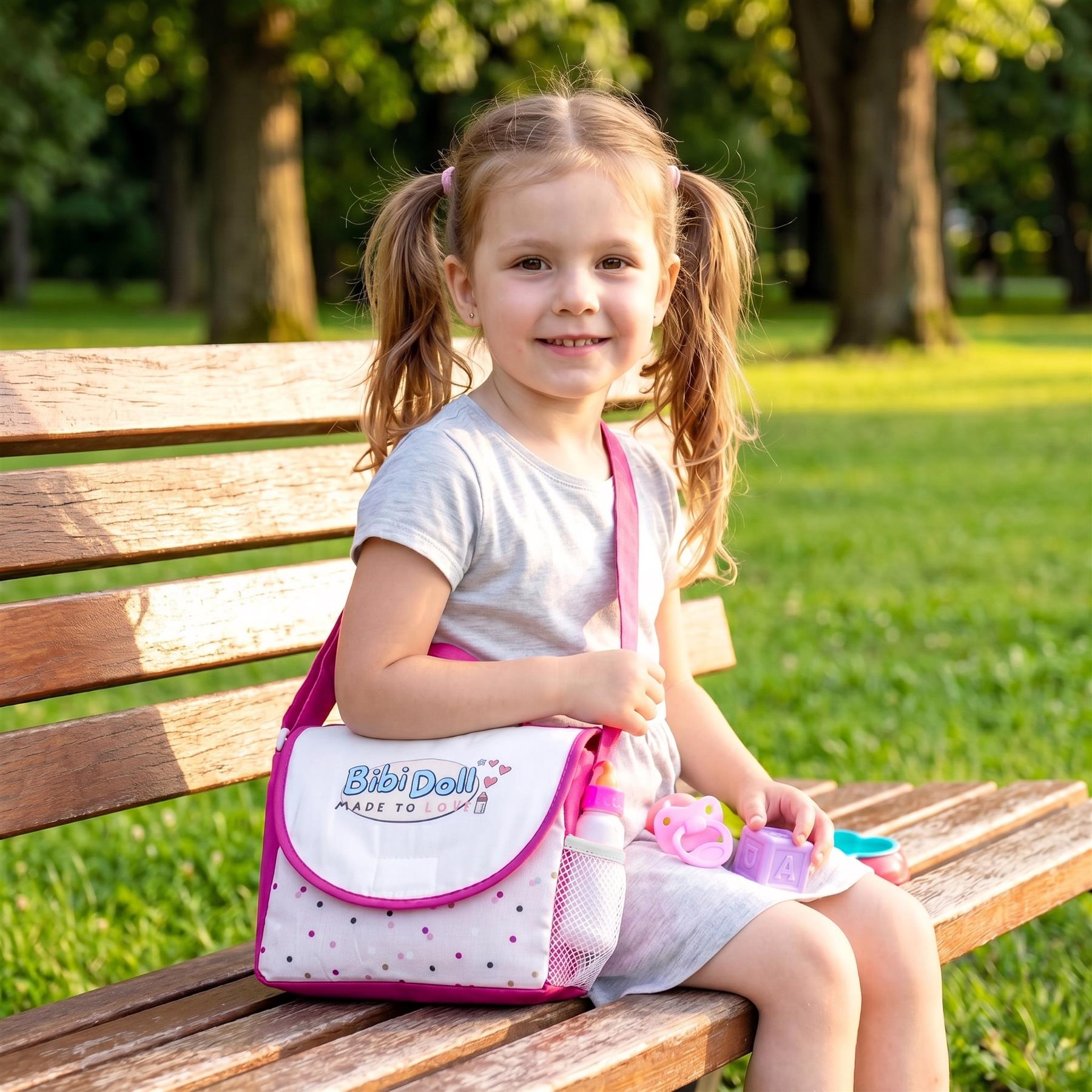 Pink patterned doll changing bag displayed with plastic accessories on a wooden park bench.