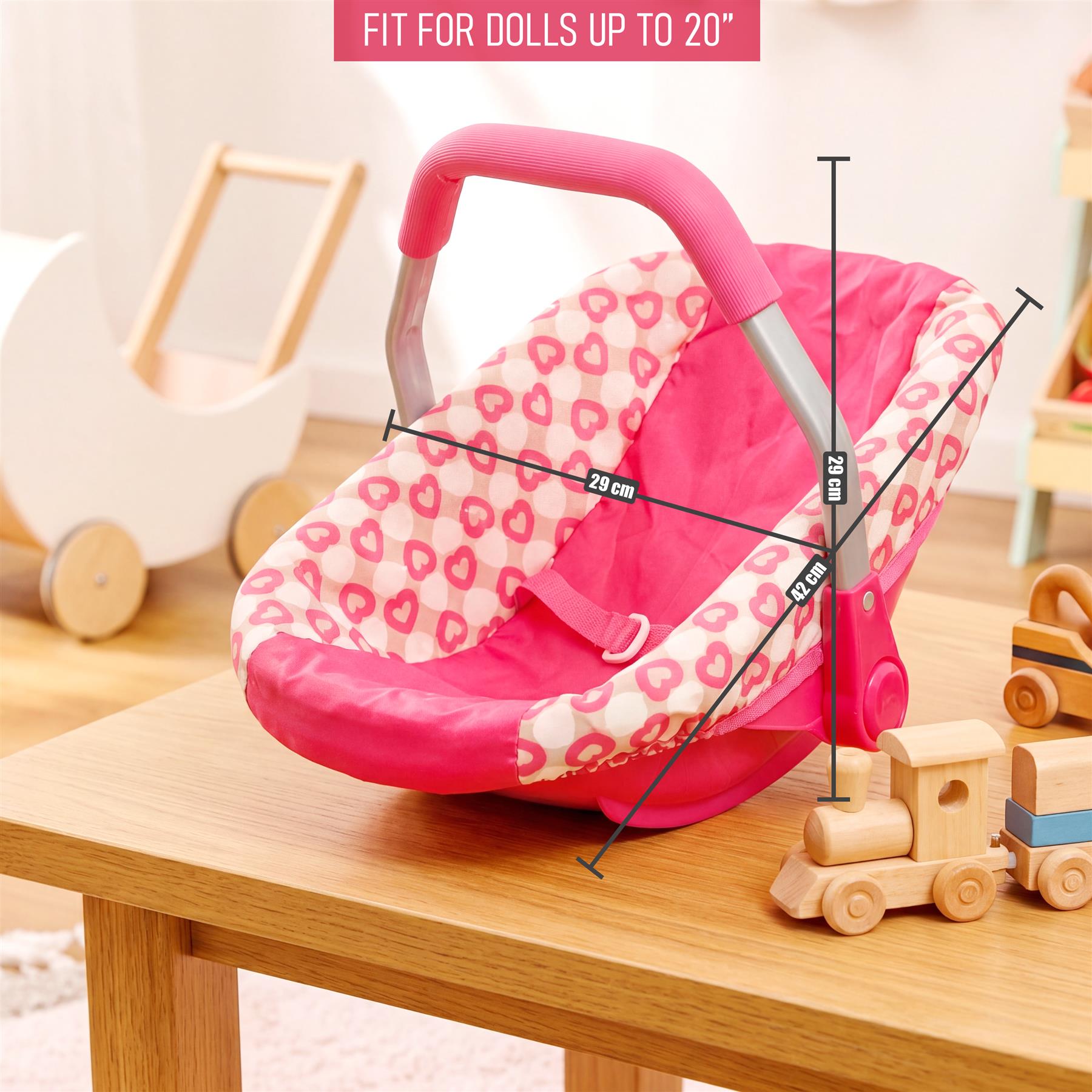 Red and white doll car seat with a pink handle sits on a wooden table.