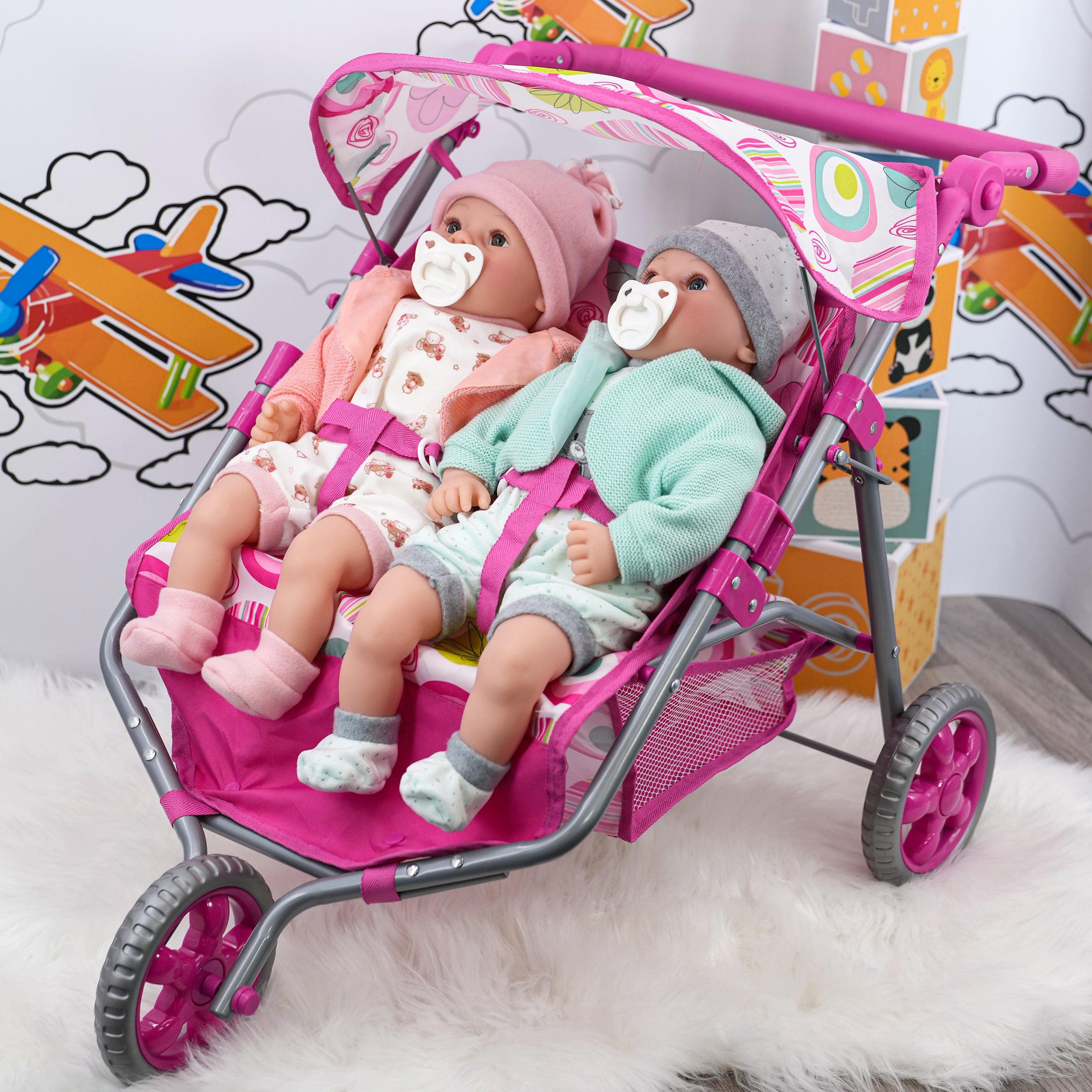 Pink three-wheeled pushchair containing two dolls dressed in coordinated outfits.