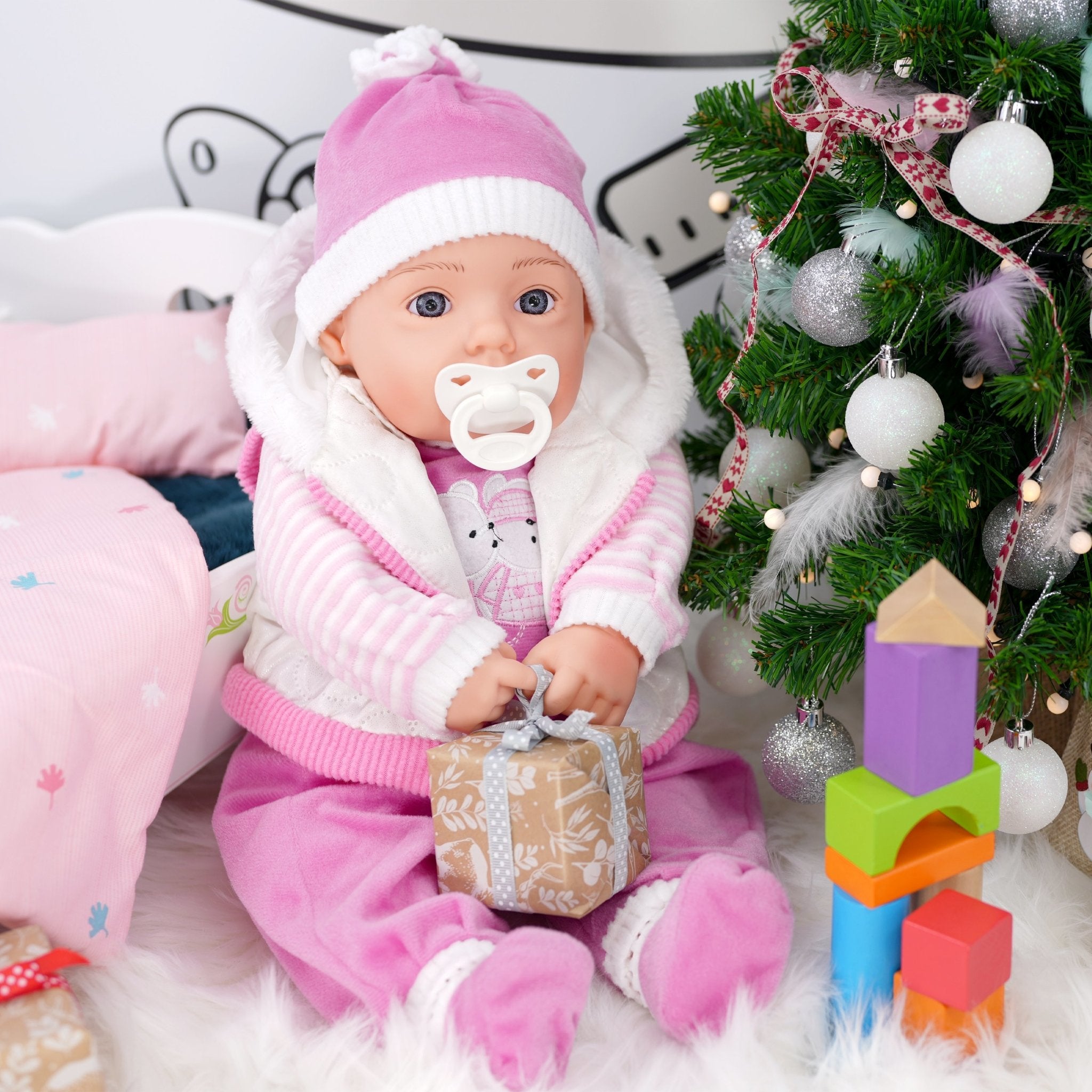 Pink baby doll in Santa outfit next to Christmas tree - The Magic Toy Shop