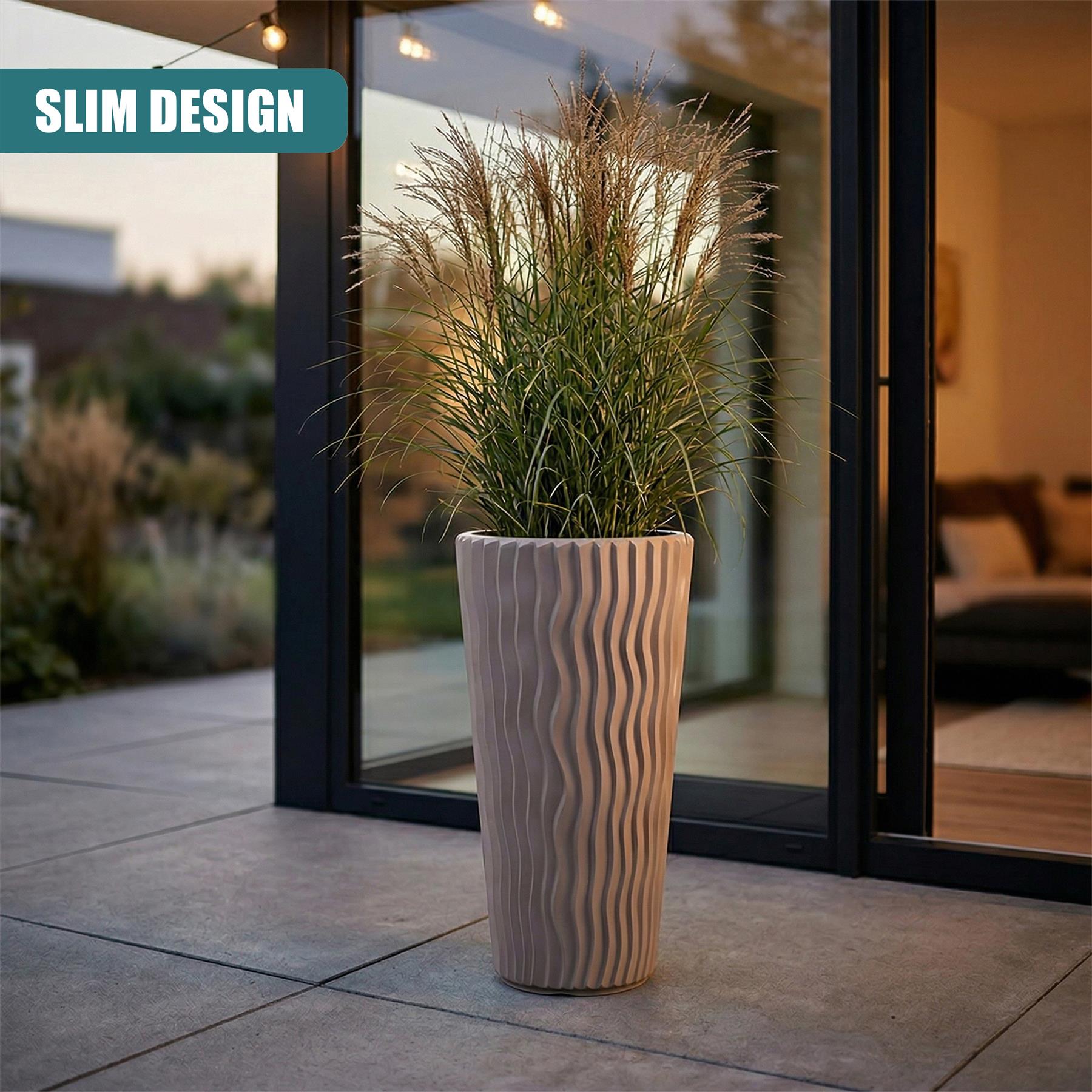 Tall, wavy brown planter pot filled with dense, wispy ornamental grass, placed by a glass door.
