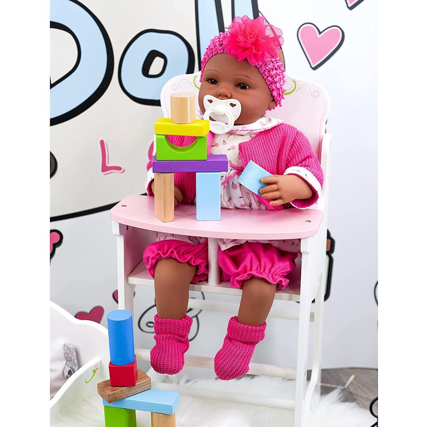 A pink doll with a toy baby in her lap sitting on a wooden high chair. The high chair has a wooden tray table, and blocks are placed on it. A stuffed animal and toy car are nearby. The backdrop has cartoonish illustrations. - The Magic Toy Shop