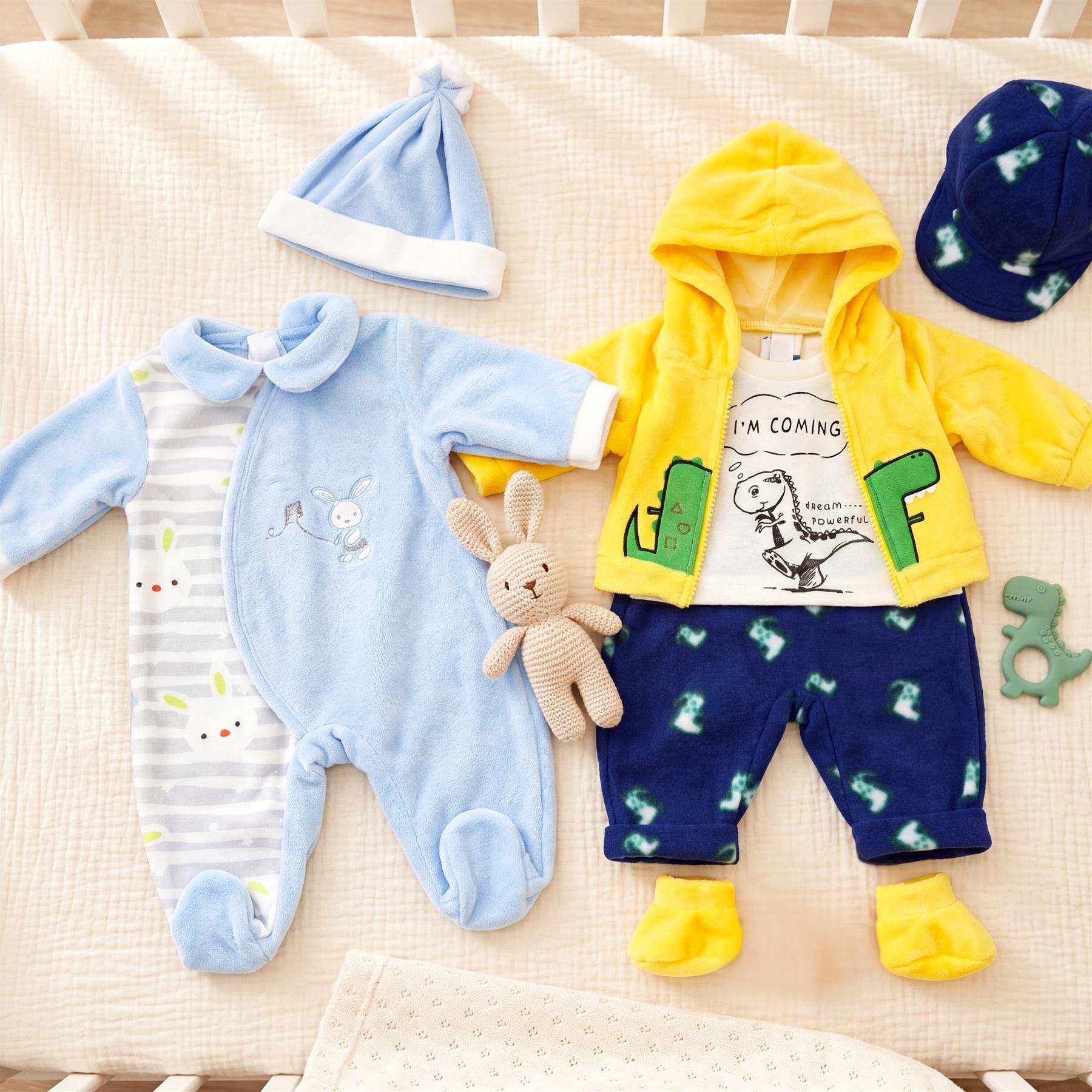 A toy clothing set featuring blue romper, yellow hoodie, and dark dinosaur print pants.