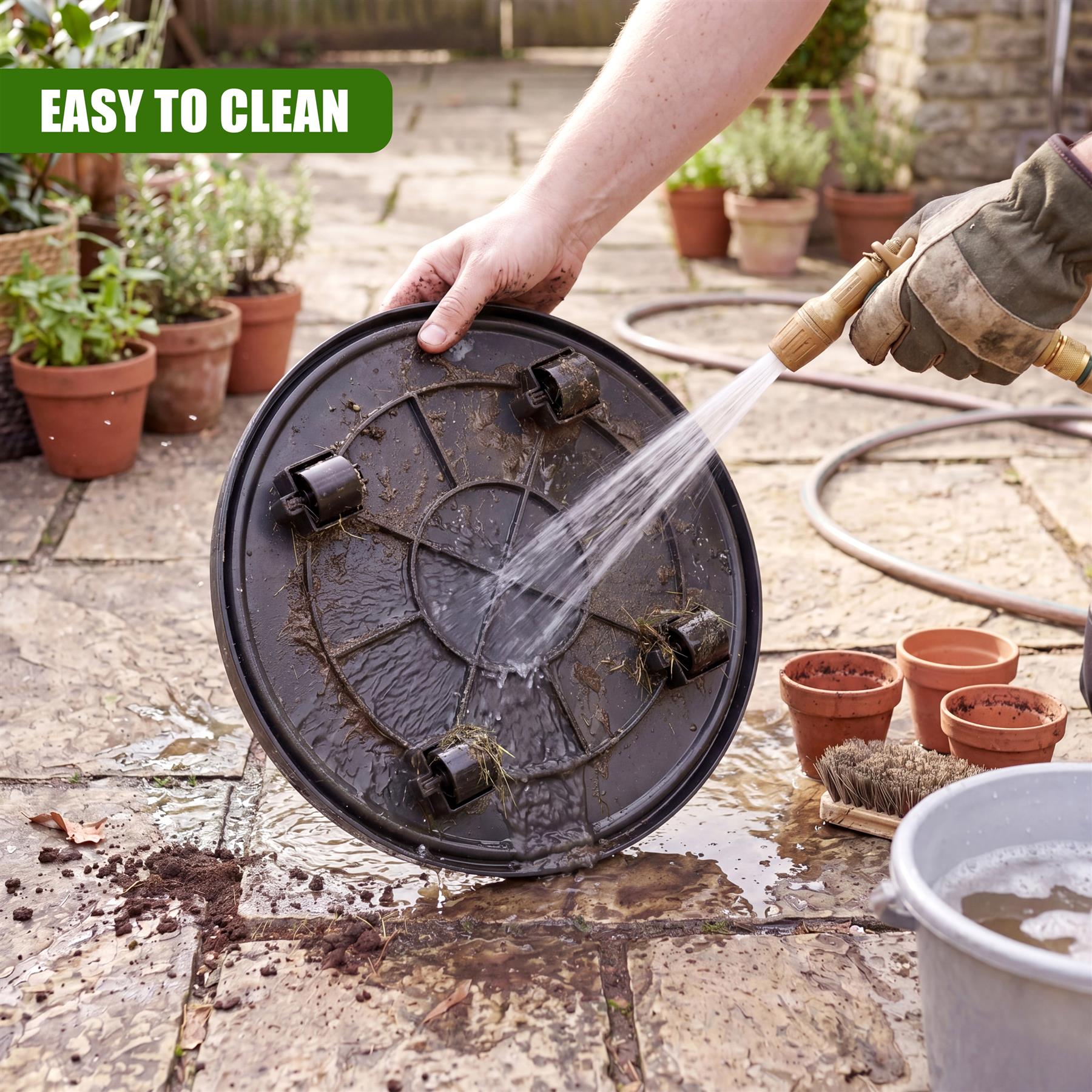 A round, dark metal plant caddy with four rollers is being sprayed with water.