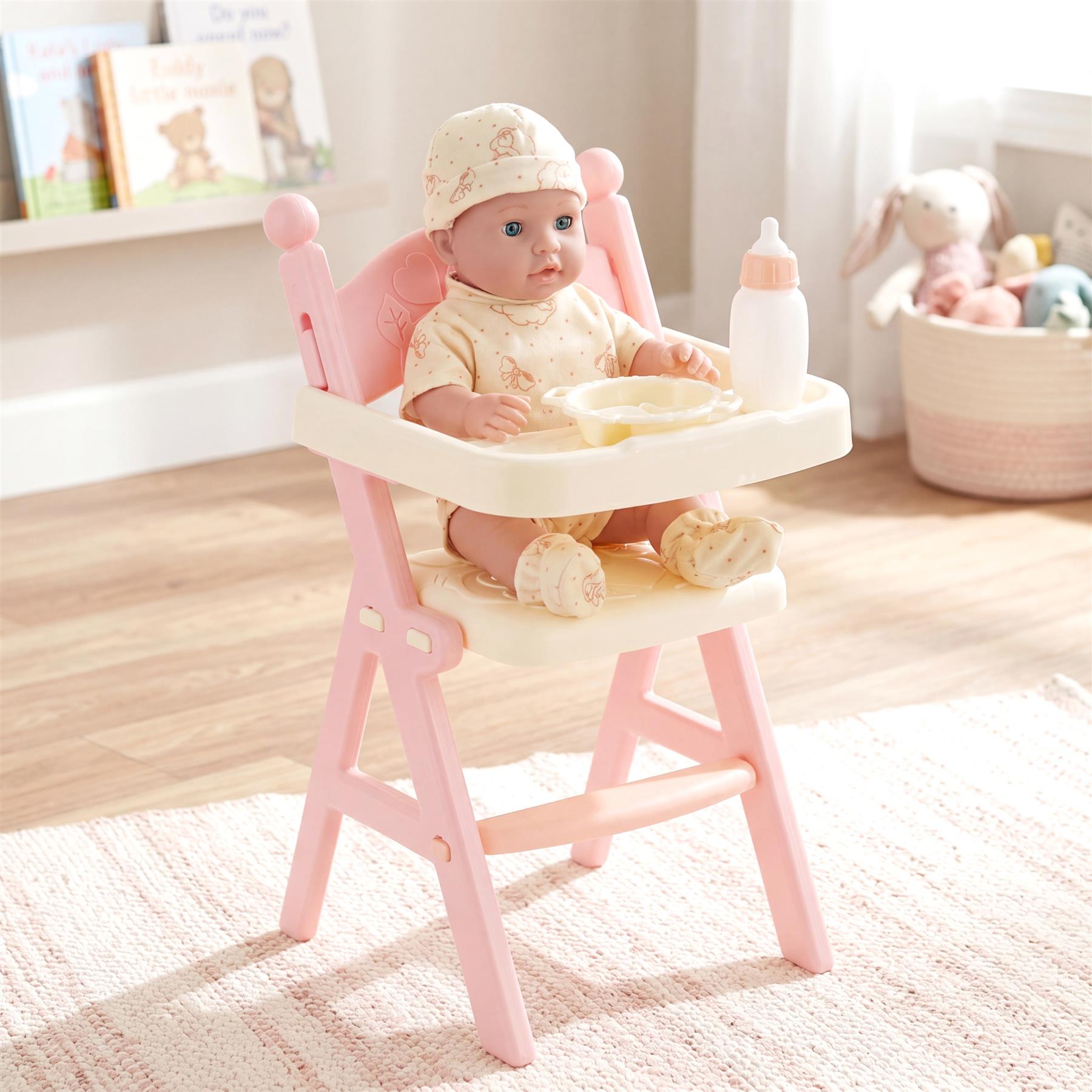 A doll sits in a pink high chair with a tray holding accessories, including a bottle and food bowl.
