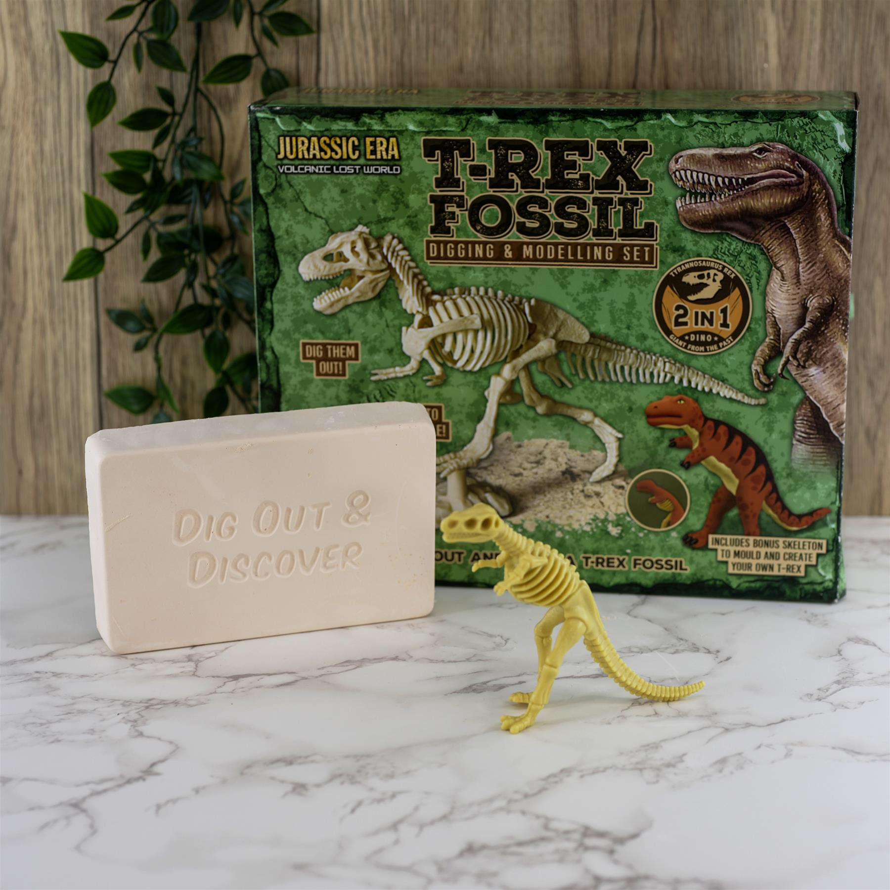 A kit box, a yellow dinosaur figure, and a pale digging block rest on a white surface.