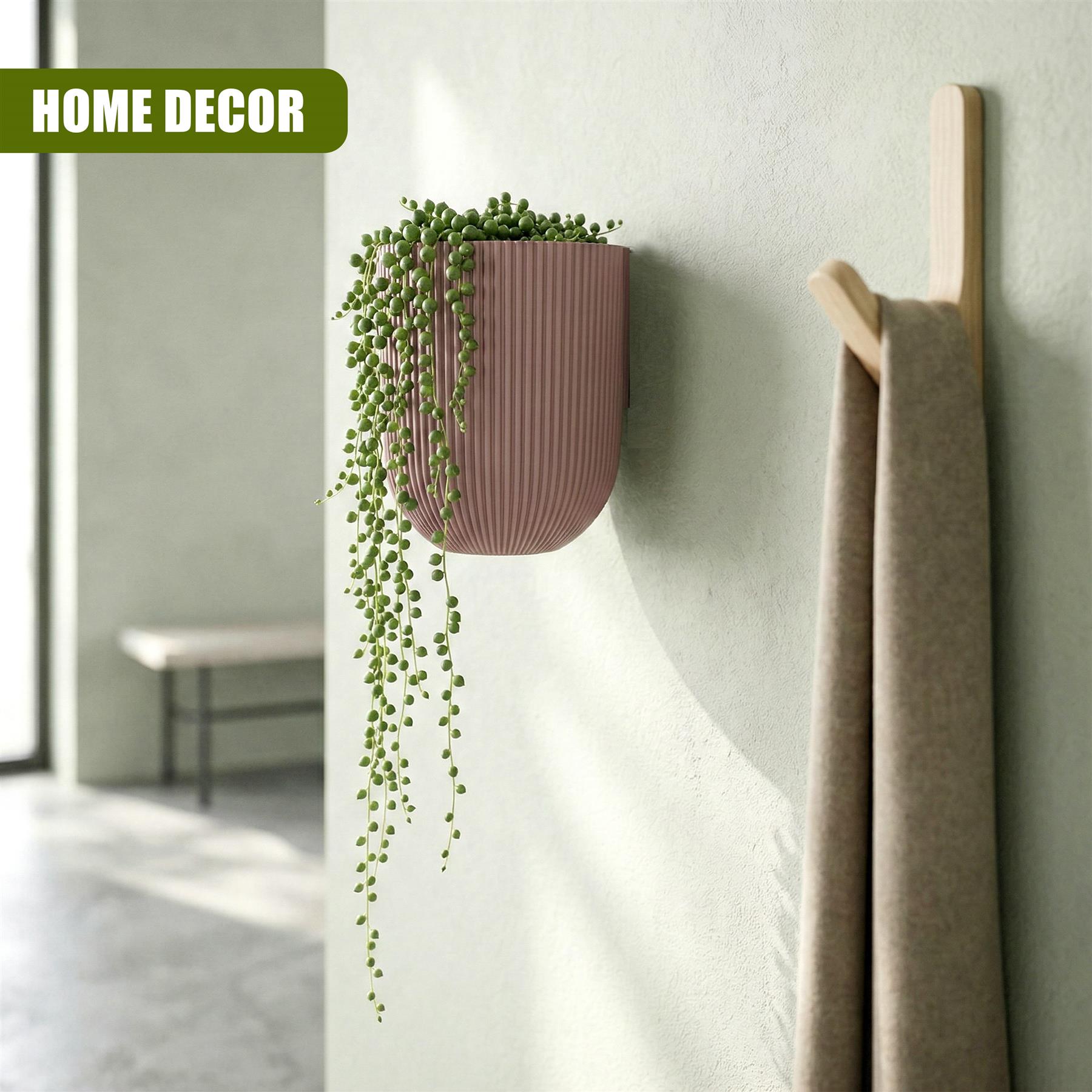 Pink wall planter with artificial trailing greenery next to a wooden towel rack holding folded towels.