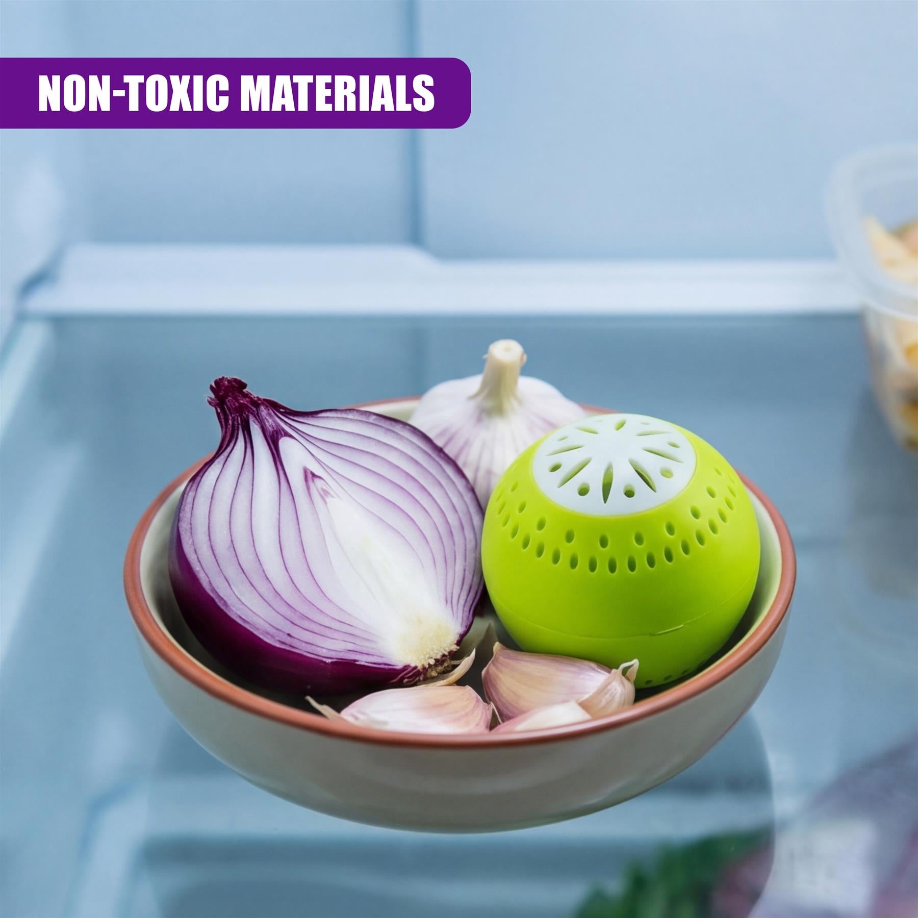 A glass bowl holds a red onion, garlic, and a porous green deodorizer resting on a shelf.