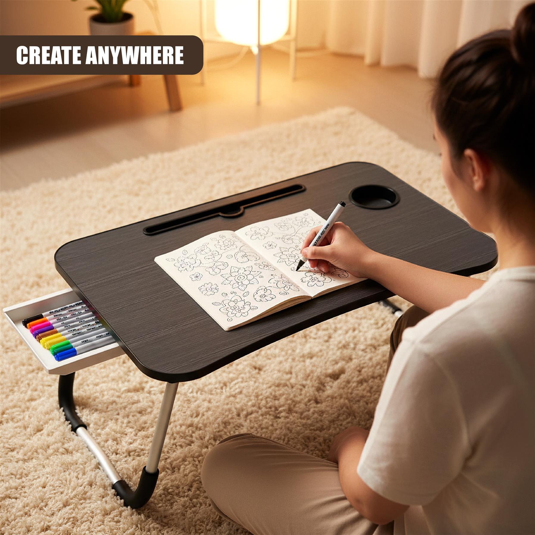 A woman sits on a rug, holding a marker and coloring in a book on a portable lap desk. The desk has a built-in cup holder and storage compartment for pens. It's a compact, versatile workspace for creative activities. - The Magic Toy Shop