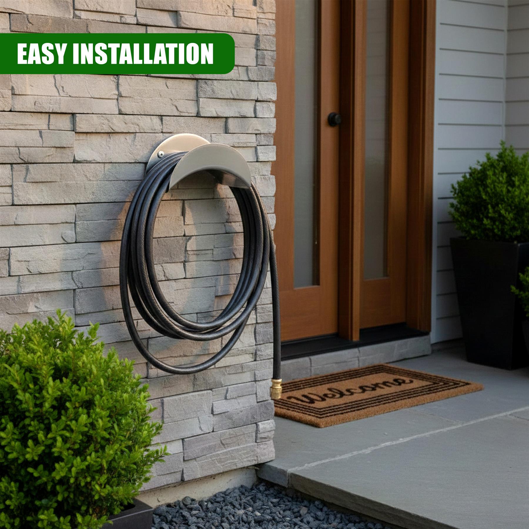 A silver curved metal holder mounts to a stone wall, supporting a coiled black garden hose.