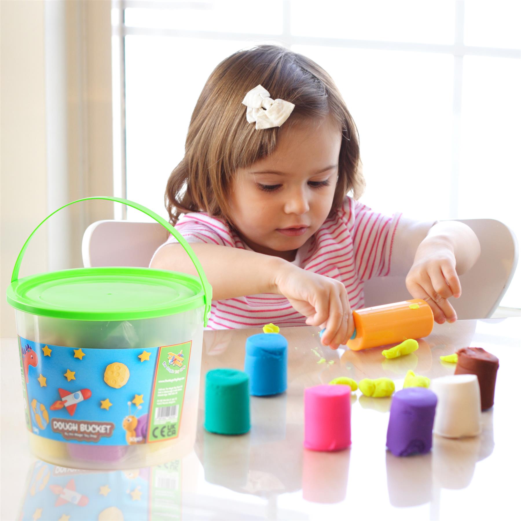 A little girl is playing with play dough, sitting at a table.