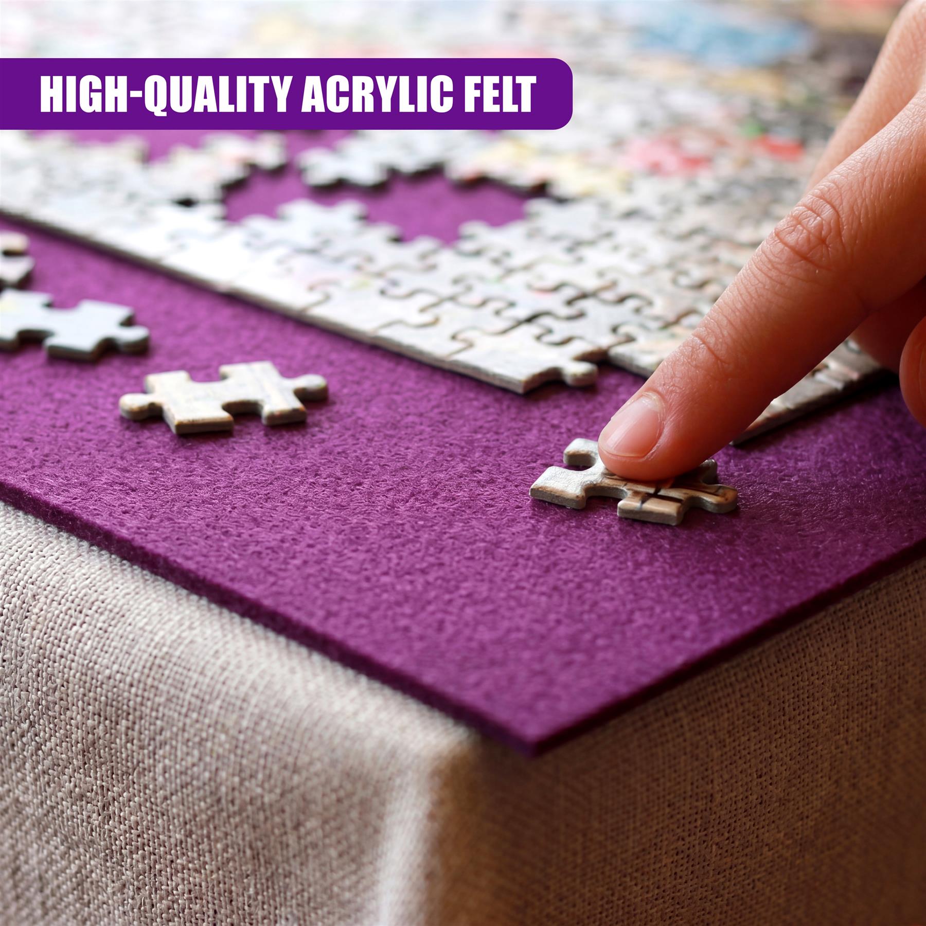 A hand handles a light puzzle piece on a purple acrylic felt mat resting on fabric.