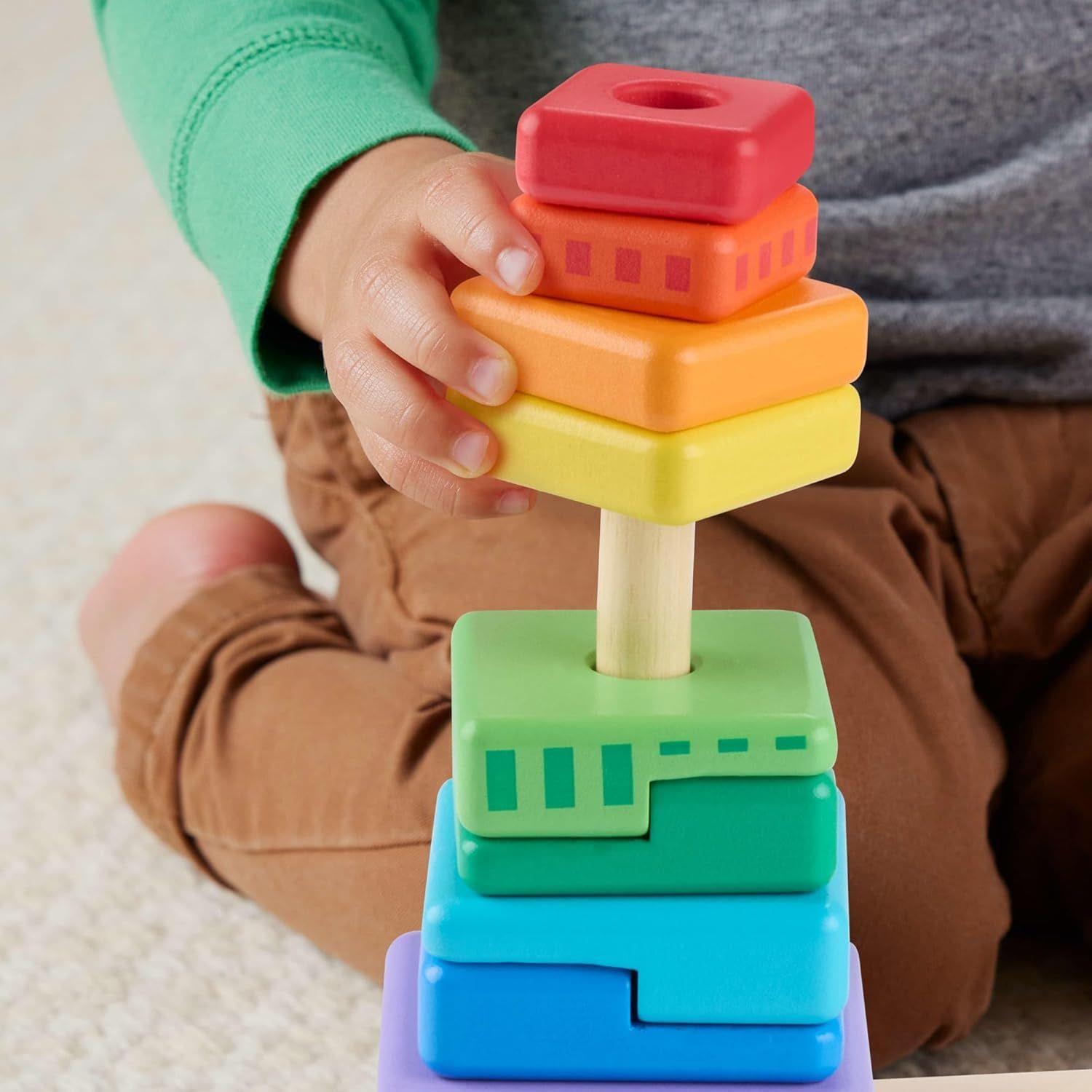 Hands stack red, orange, yellow blocks onto a colorful wooden stacking toy tower.