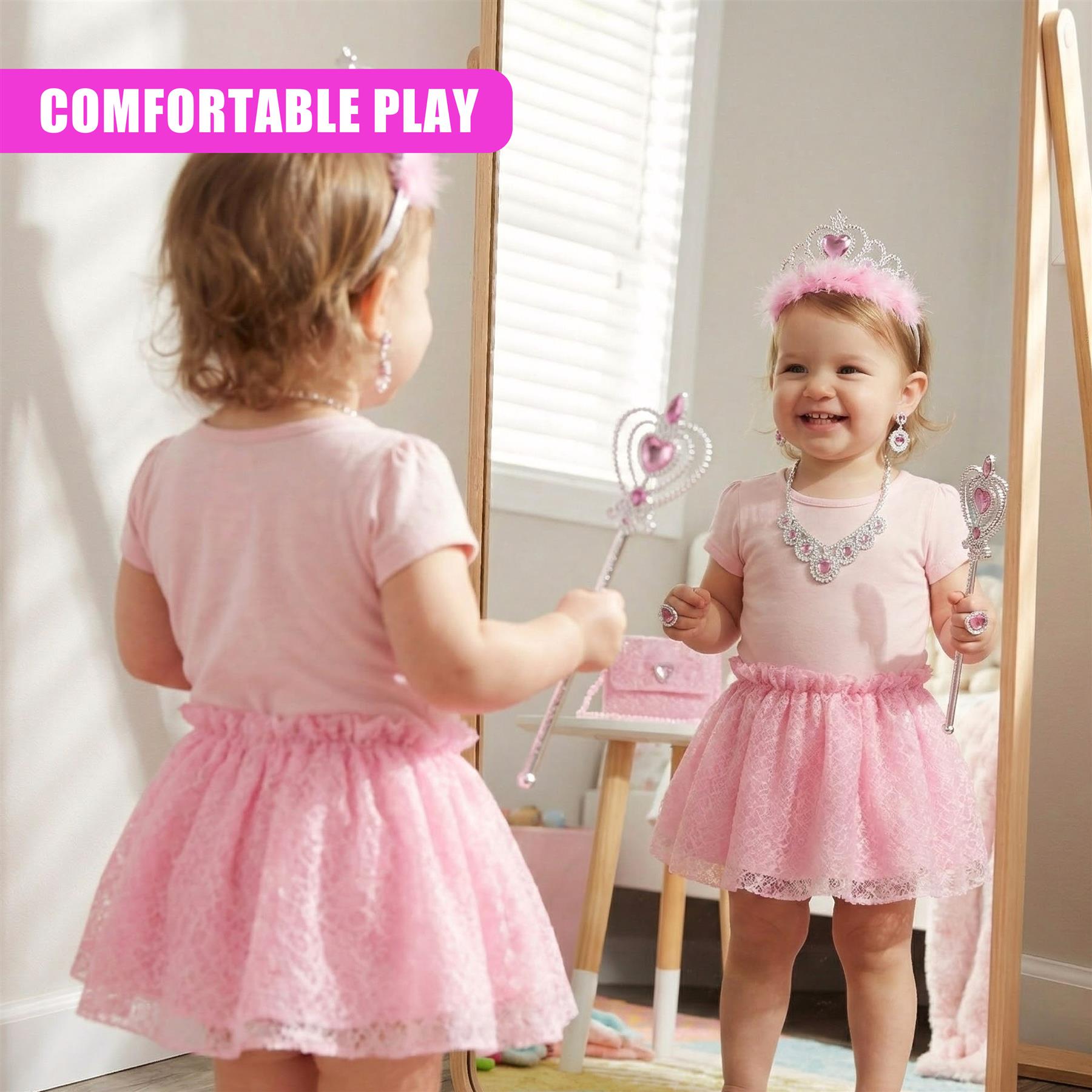 A young girl in a pink dress, holding a toy wand and smiling at her reflection in a mirror. The room is decorated with a pink and white theme, with a pink chair and a white table in the background. The girl is wearing a pink crown and a pink dress with a white flower. - The Magic Toy Shop