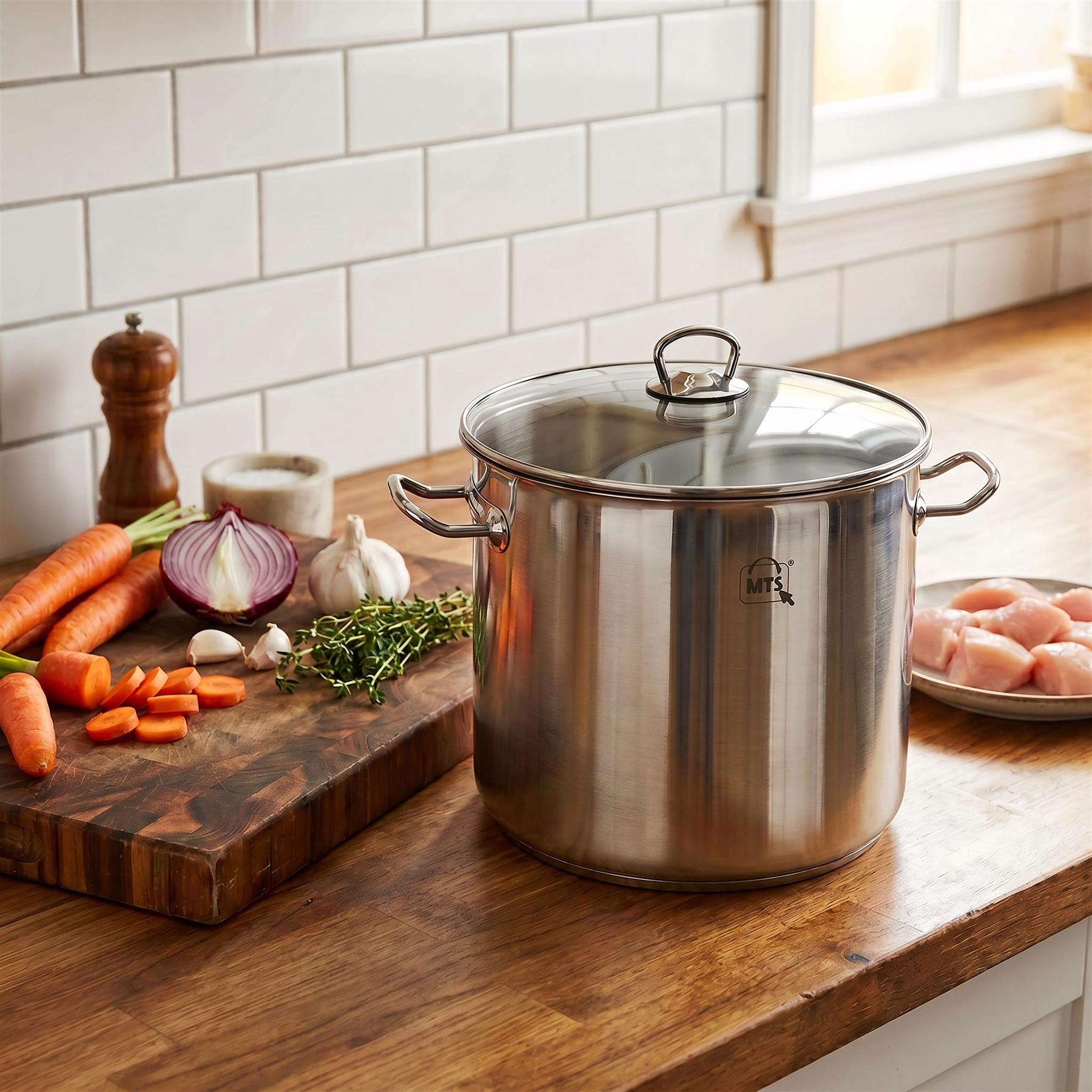 Stainless steel stock pot sits on wood counter next to raw ingredients like carrots and garlic.