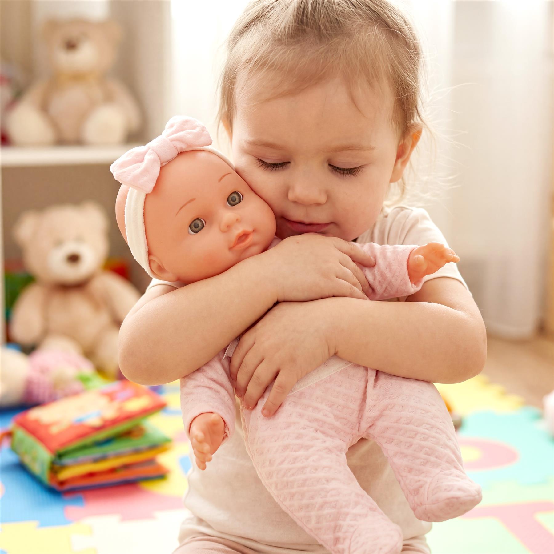 Young girl cradles a baby doll wearing a bow and wrapped in soft pink cloth.