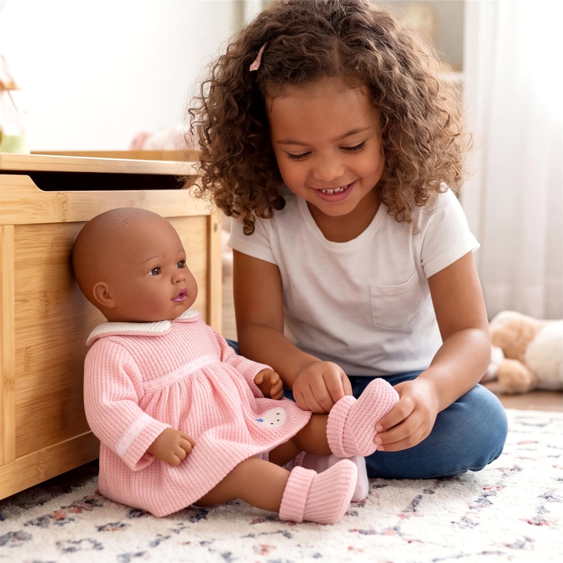 Girl plays with a doll wearing a pink dress while holding small, coordinating pink booties.