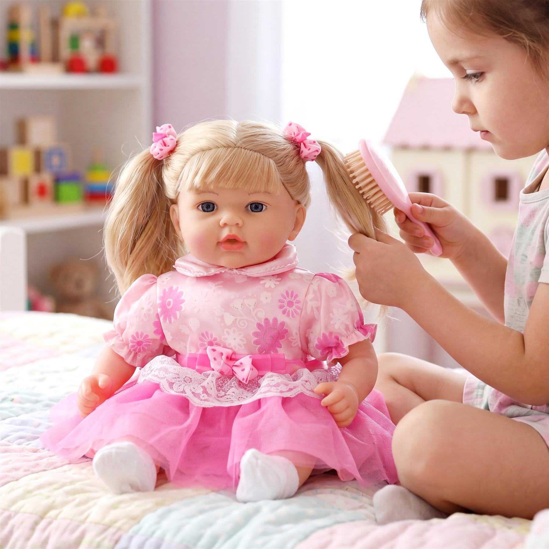 Child brushing a blonde baby doll's hair, which is dressed in a pink floral outfit.