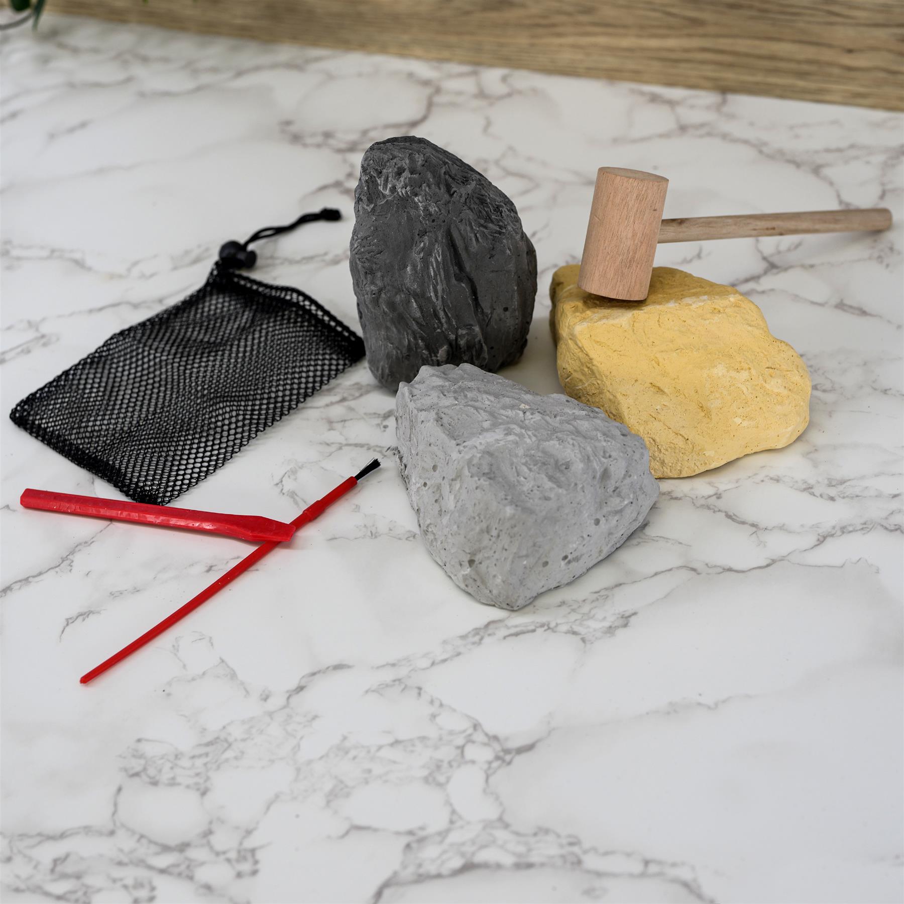 Black mesh bag, red tool, three stones of varying color, and a wooden mallet on a marbled surface.