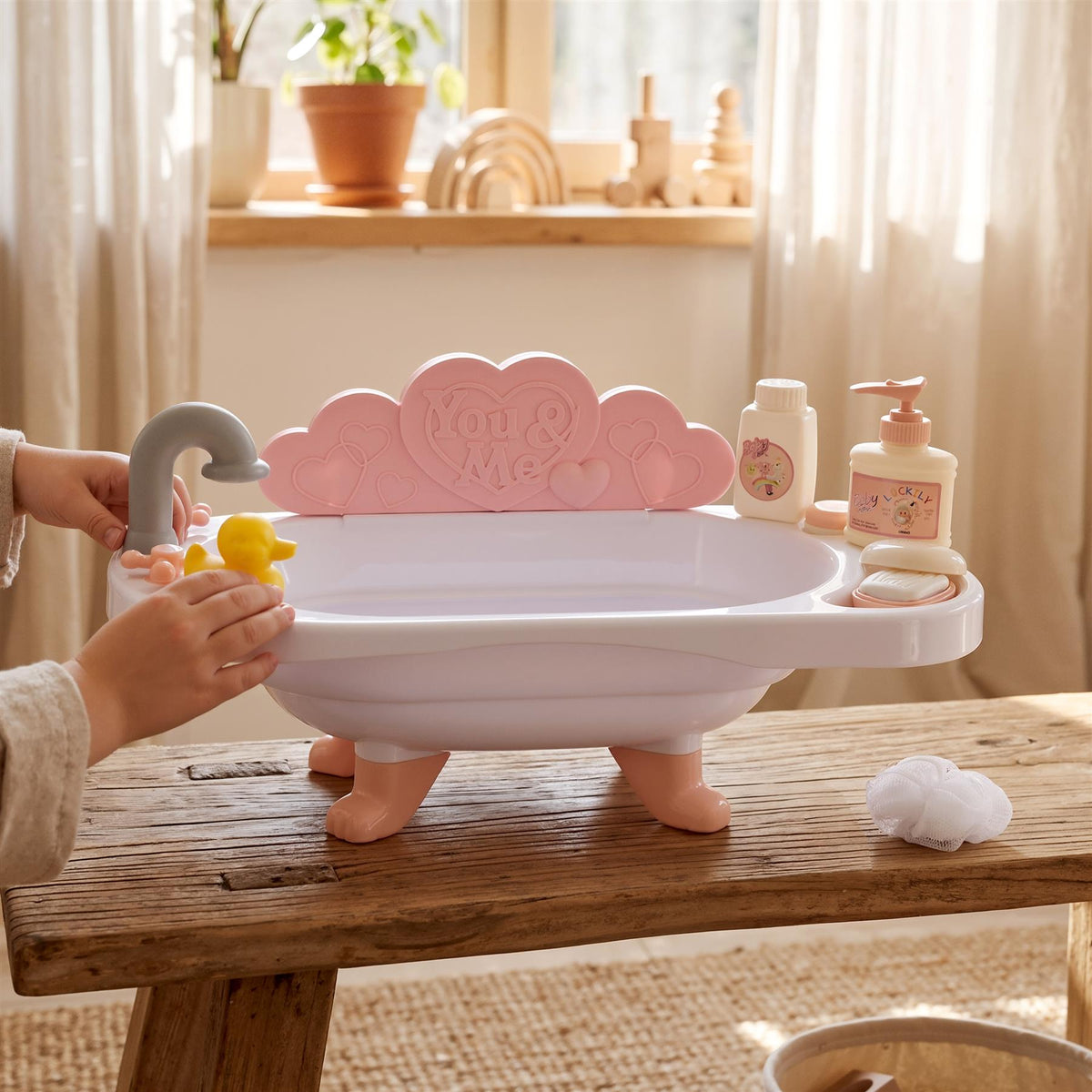 Pink doll bath set with accessories, including a bathtub and duck, on a wooden surface