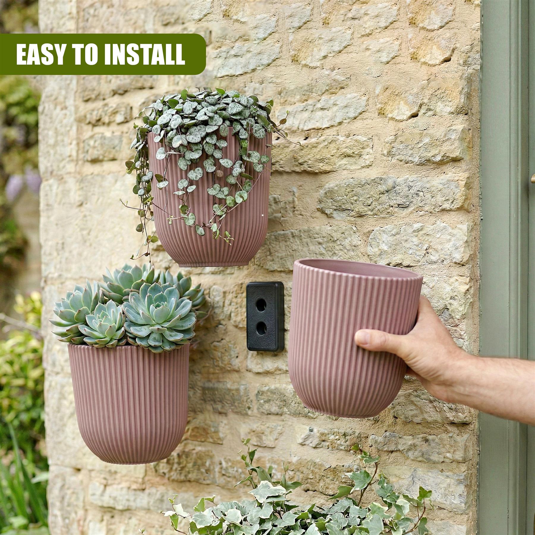 Two light pink planters, one with succulents and one empty, are displayed on a natural stone wall.