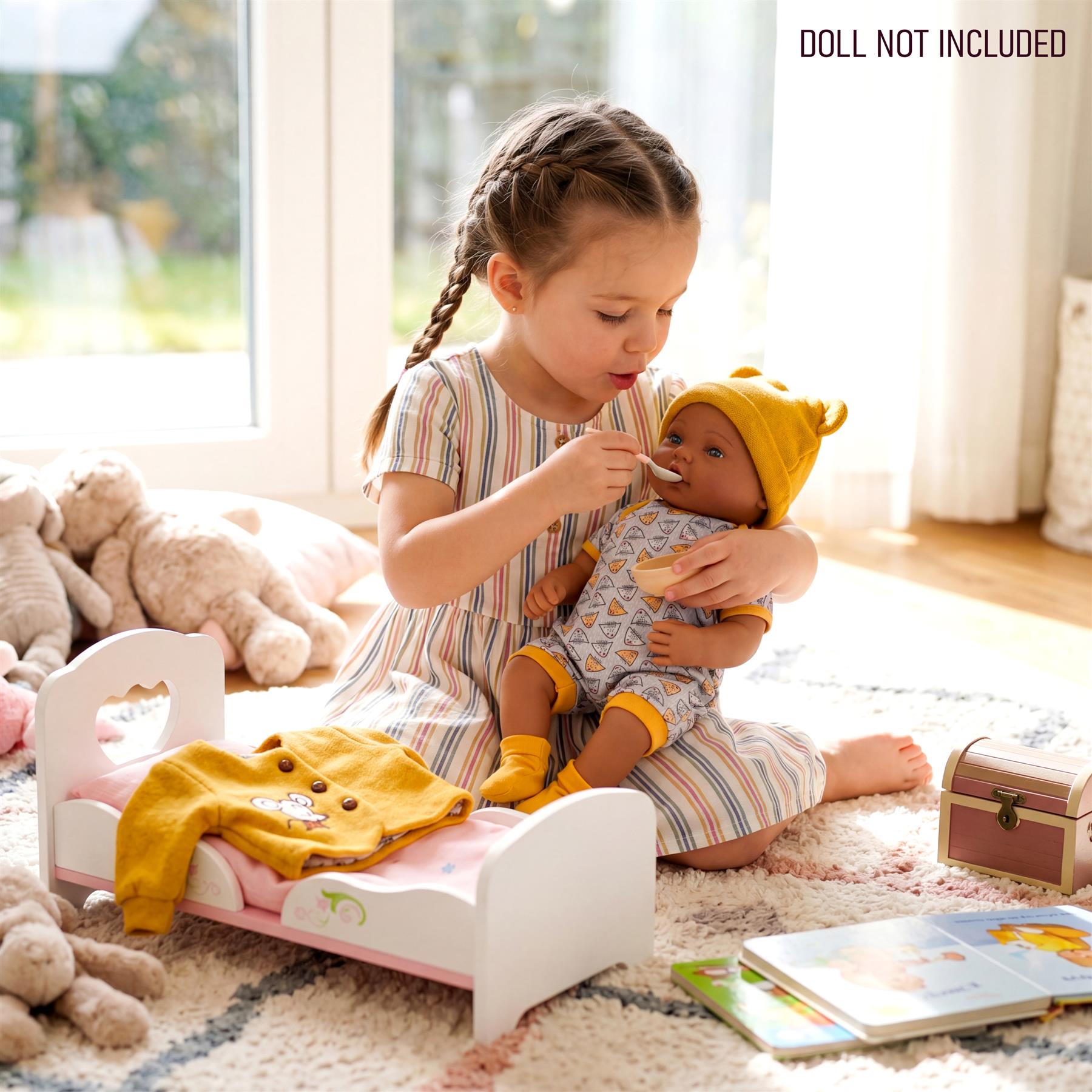 Girl interacts with a doll wearing a hat near a pink crib and yellow outfit accessory.
