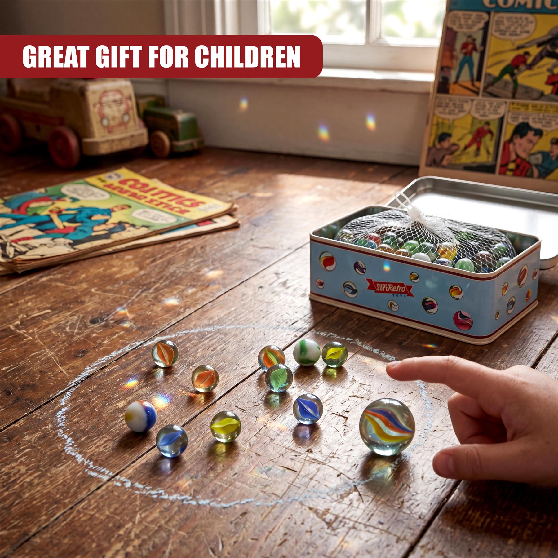 Hand near scattered marbles and an open tin box on a wooden surface next to comic books.