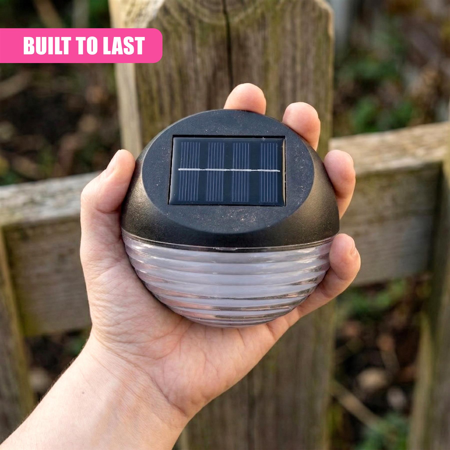A hand holds a black solar light fixture with a visible panel and ribbed body.