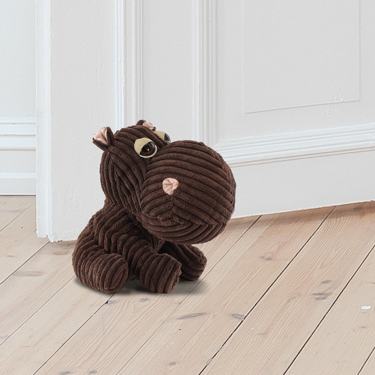Brown ribbed hippo doorstop sits on a wooden floor next to a white door